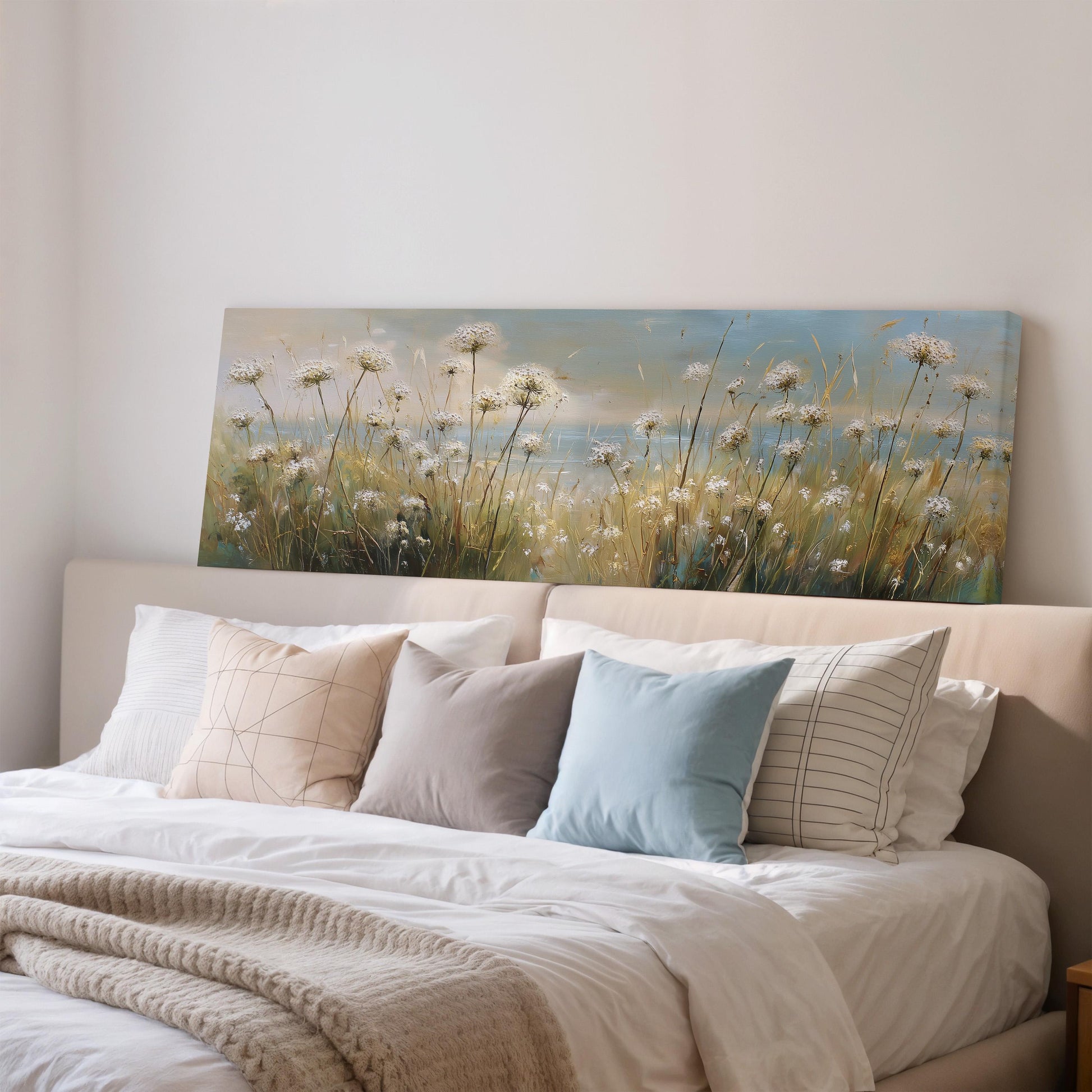 a large painting of a field of flowers hanging above a bed with white pillows and a gray blanket.
