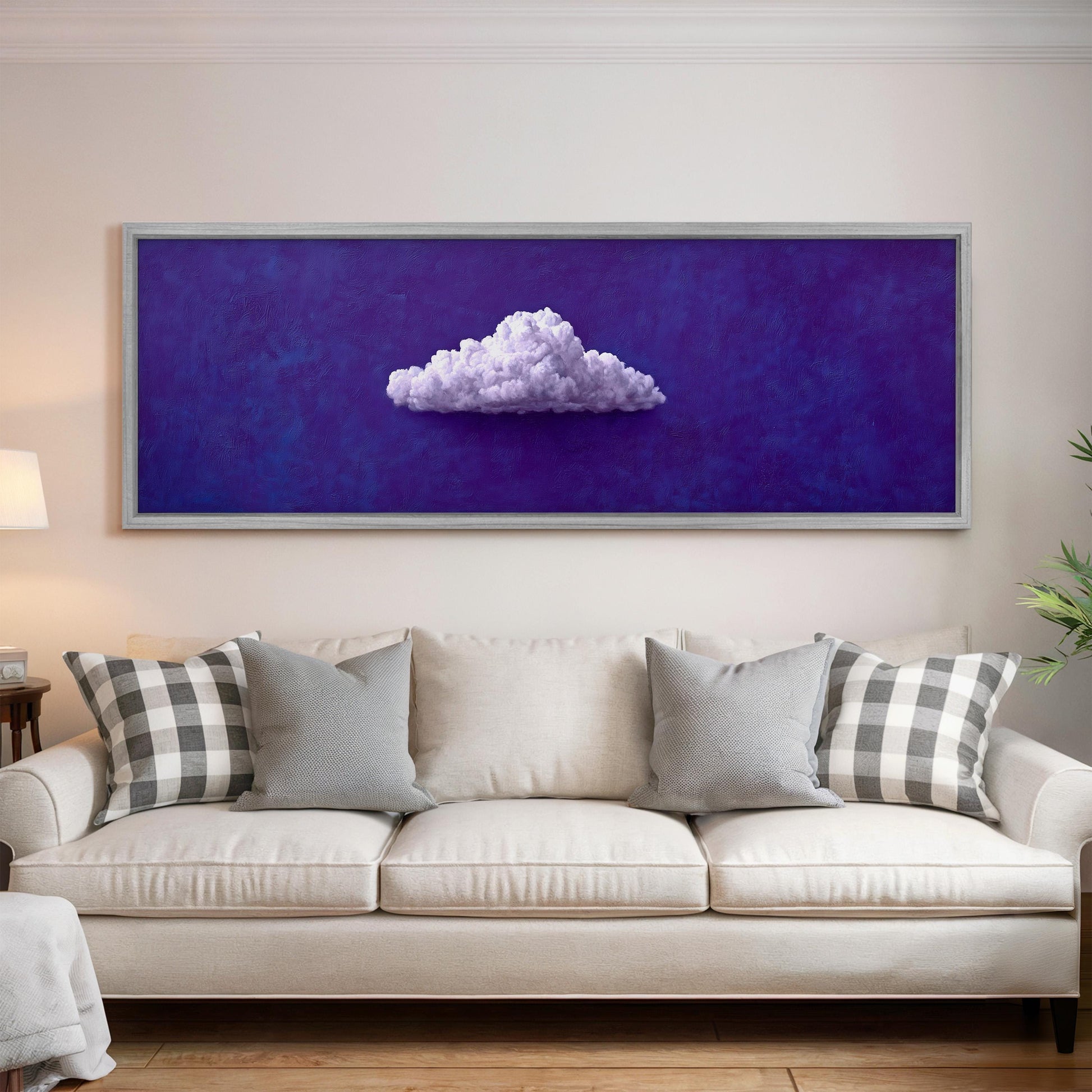 a large, framed painting of a cloud on a purple background hanging on a wall above a white couch with gray and white patterned pillows.