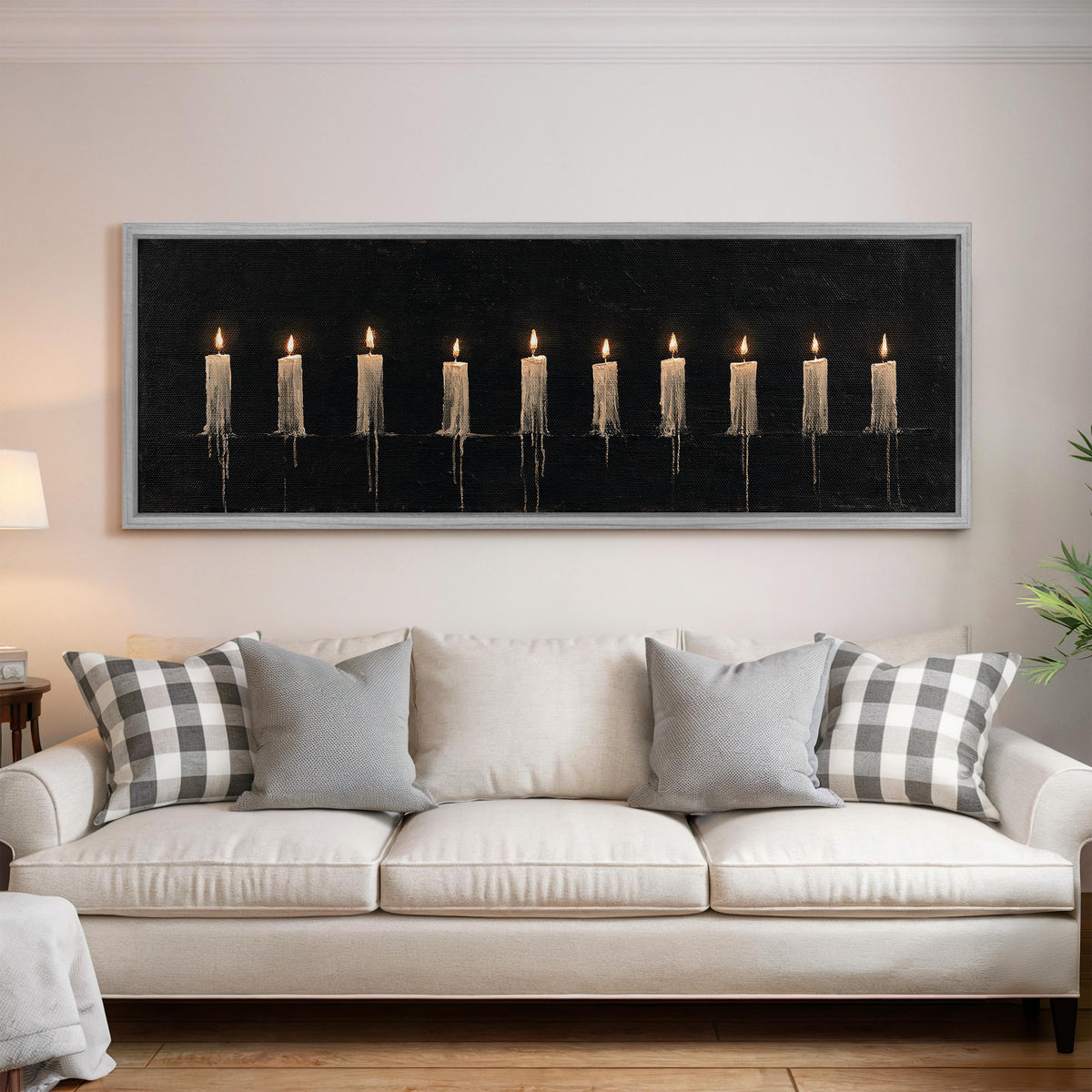 Ten lit candles on black panoramic canvas print above a white sofa in a bright living room
