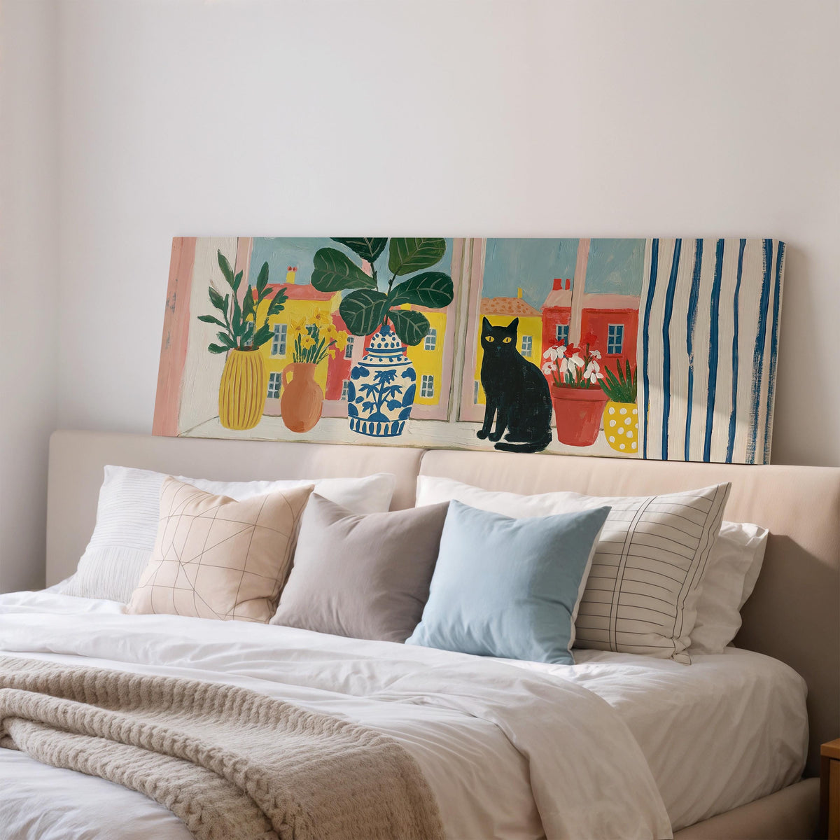 Black cat on a windowsill overlooking a colorful village wide panoramic canvas print above a bed in a bedroom