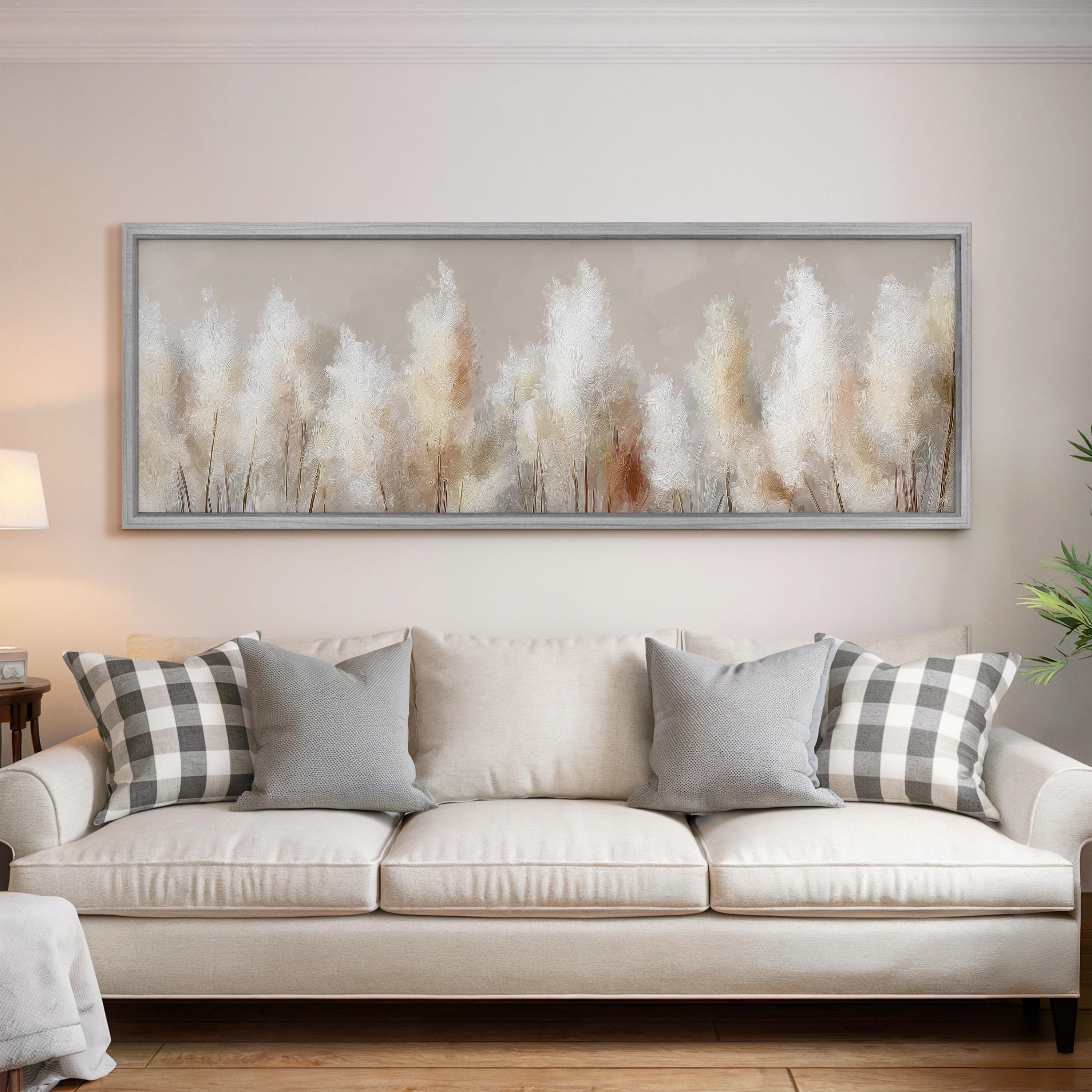 a large, white couch with gray and black plaid throw pillows, set against a wall with a framed painting of tall grasses.