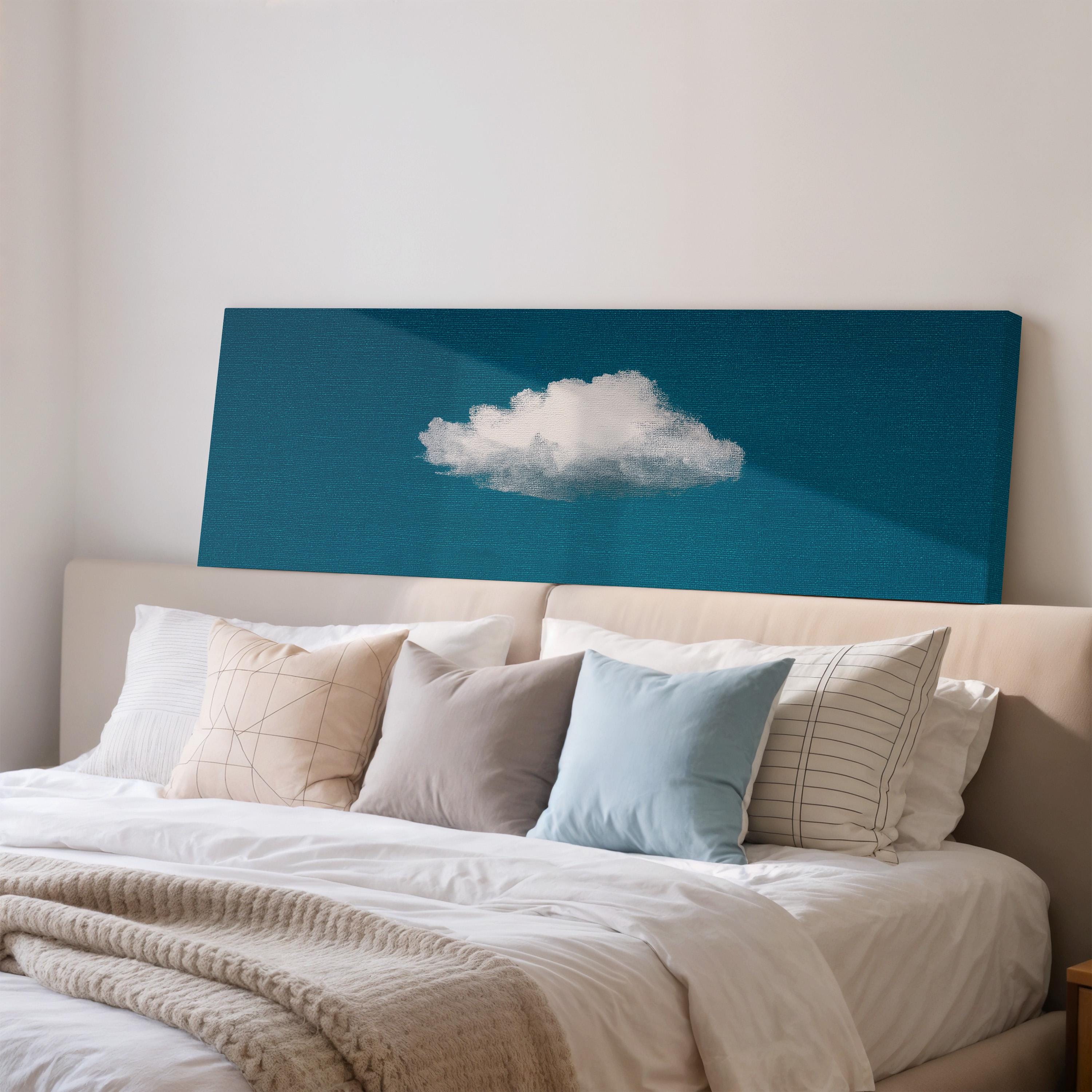 a cozy bedroom with a bed adorned with white pillows and a gray throw blanket. Above the bed, there is a blue canvas with a white cloud design, creating a serene and calming atmosphere.