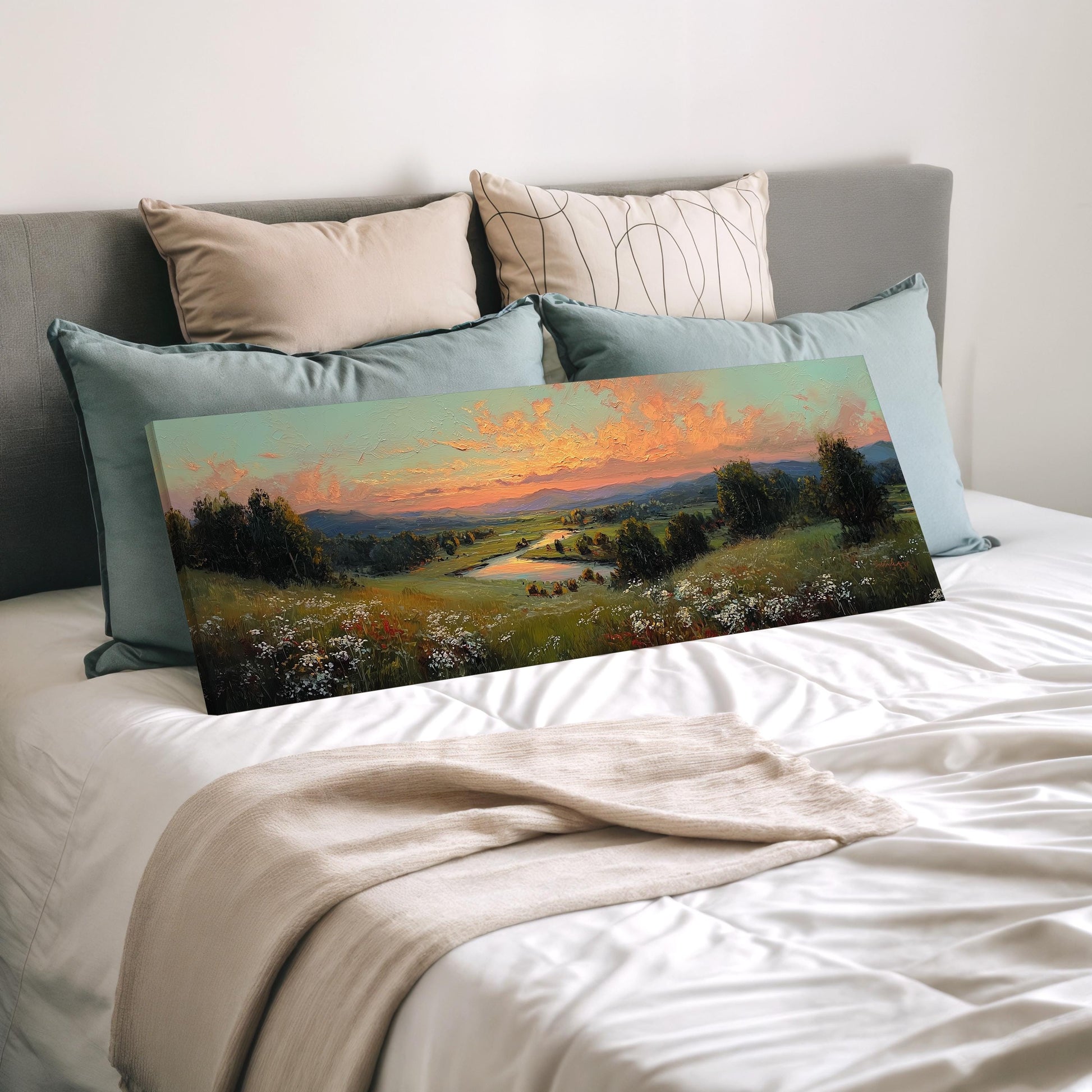 a large landscape painting displayed on a bed, with a beige blanket and pillows surrounding it.