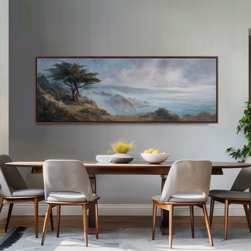 a dining room with a large painting of a landscape hanging on the wall above a wooden table with four chairs. The painting depicts a serene scene of a tree overlooking a body of water, with mountains in the background. The table is set with a bowl of fruit and a vase of flowers, creating a cozy and inviting atmosphere.