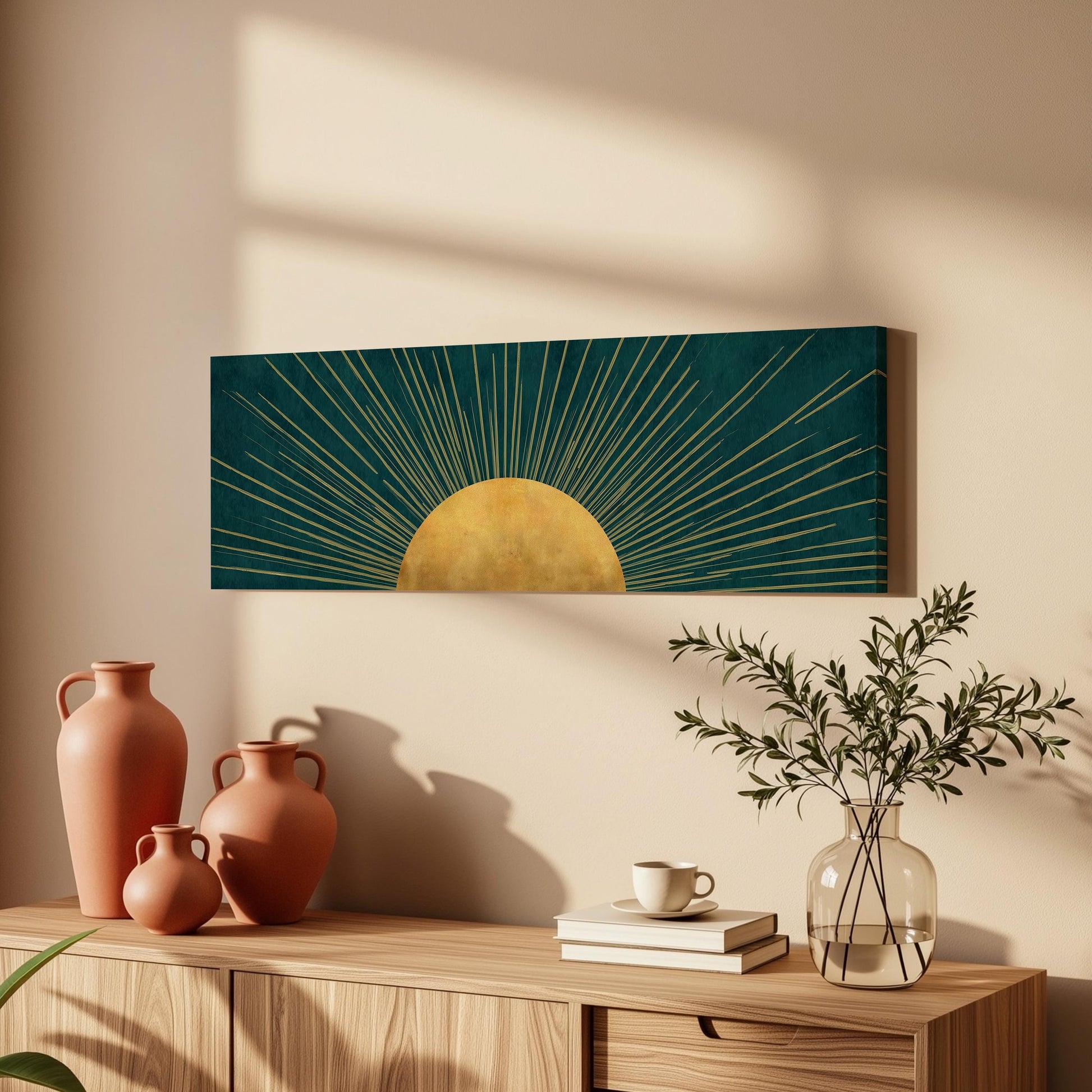 a wooden cabinet with a vase, a coffee cup, and a stack of books on top. Above the cabinet, there is a framed artwork depicting a sun with rays radiating from it.