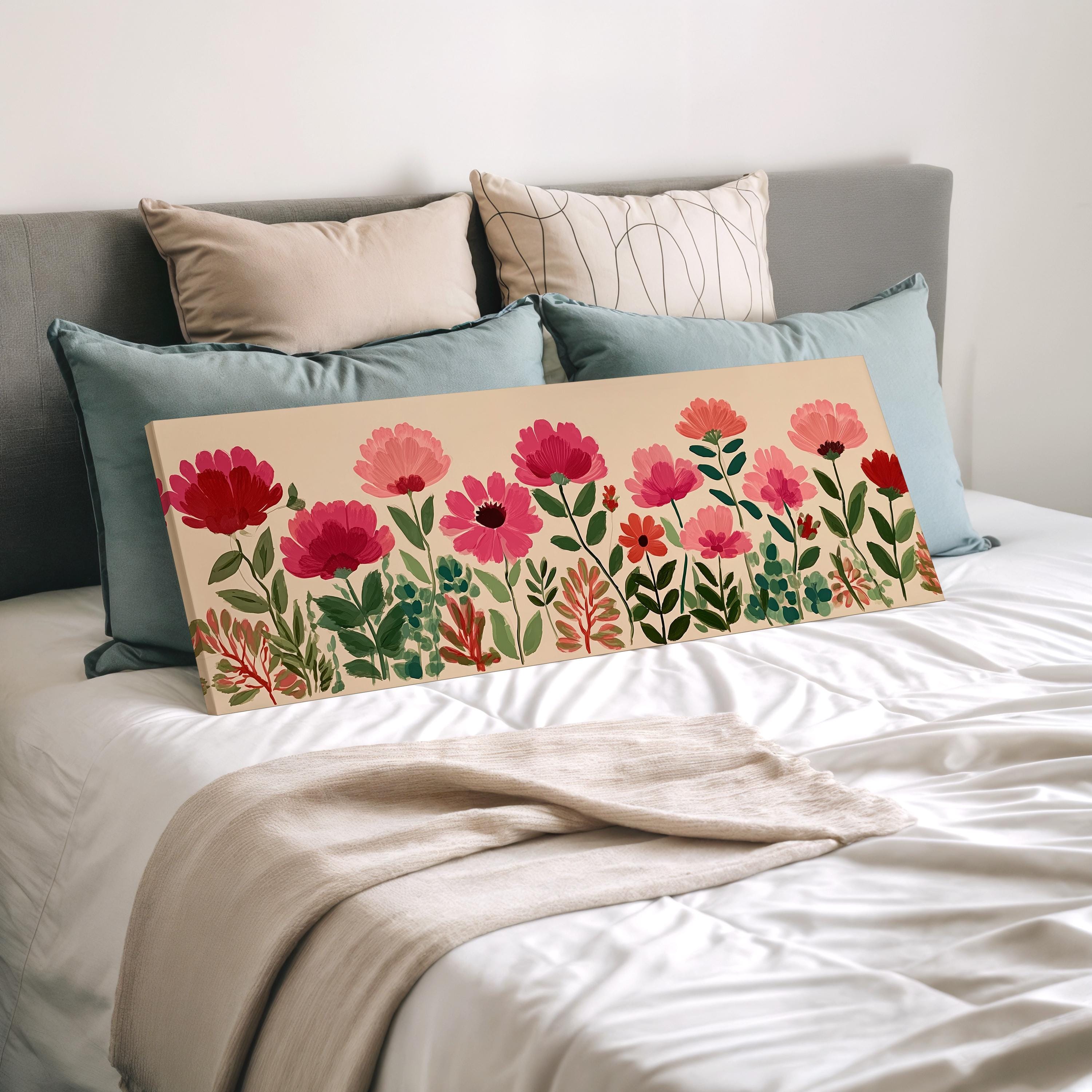 a bed with a white comforter and a large floral print on the bed. The print features pink flowers and green leaves. The bed is surrounded by various pillows, creating a cozy and inviting atmosphere.