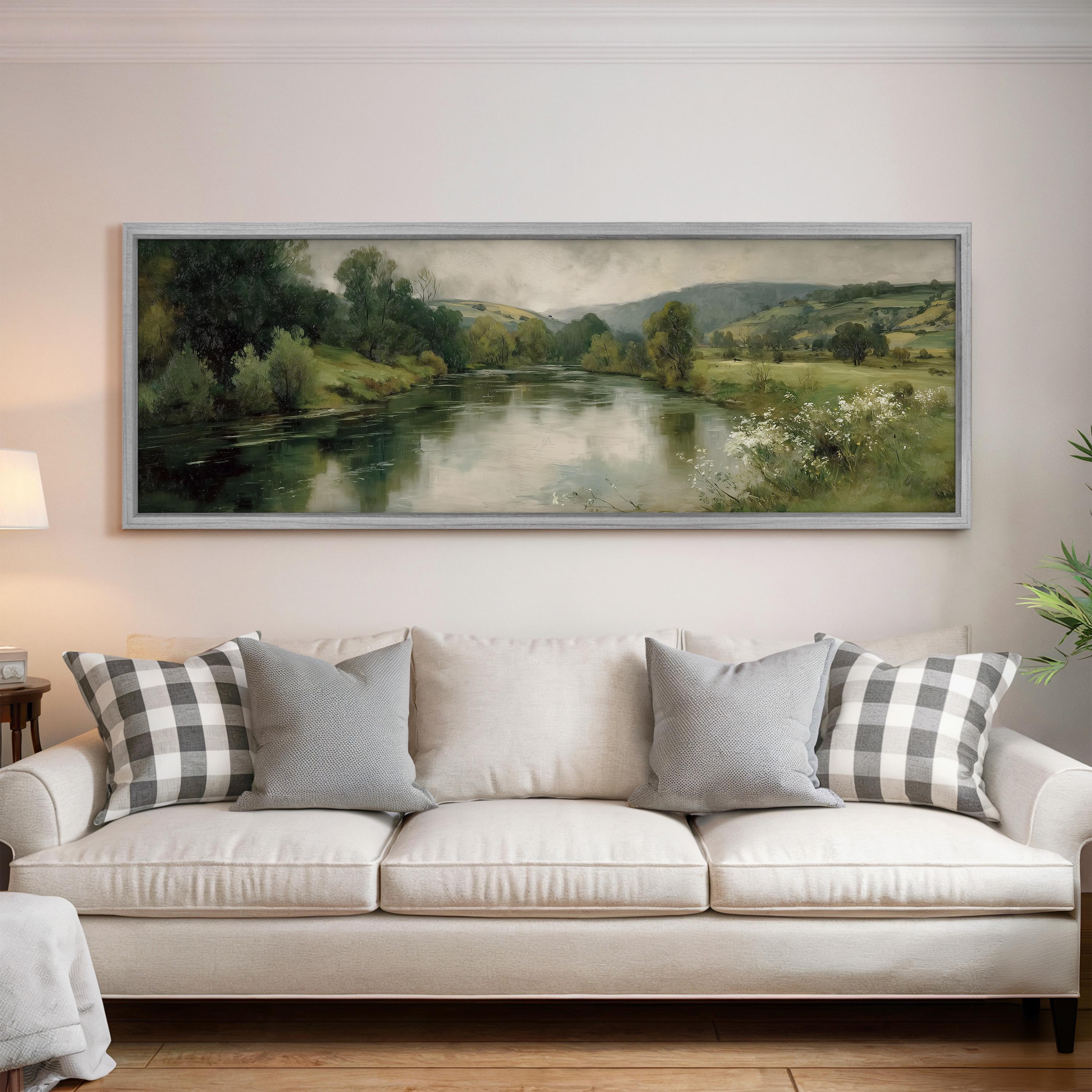 a large painting of a serene landscape hanging on a wall above a white sofa with gray and white patterned pillows.