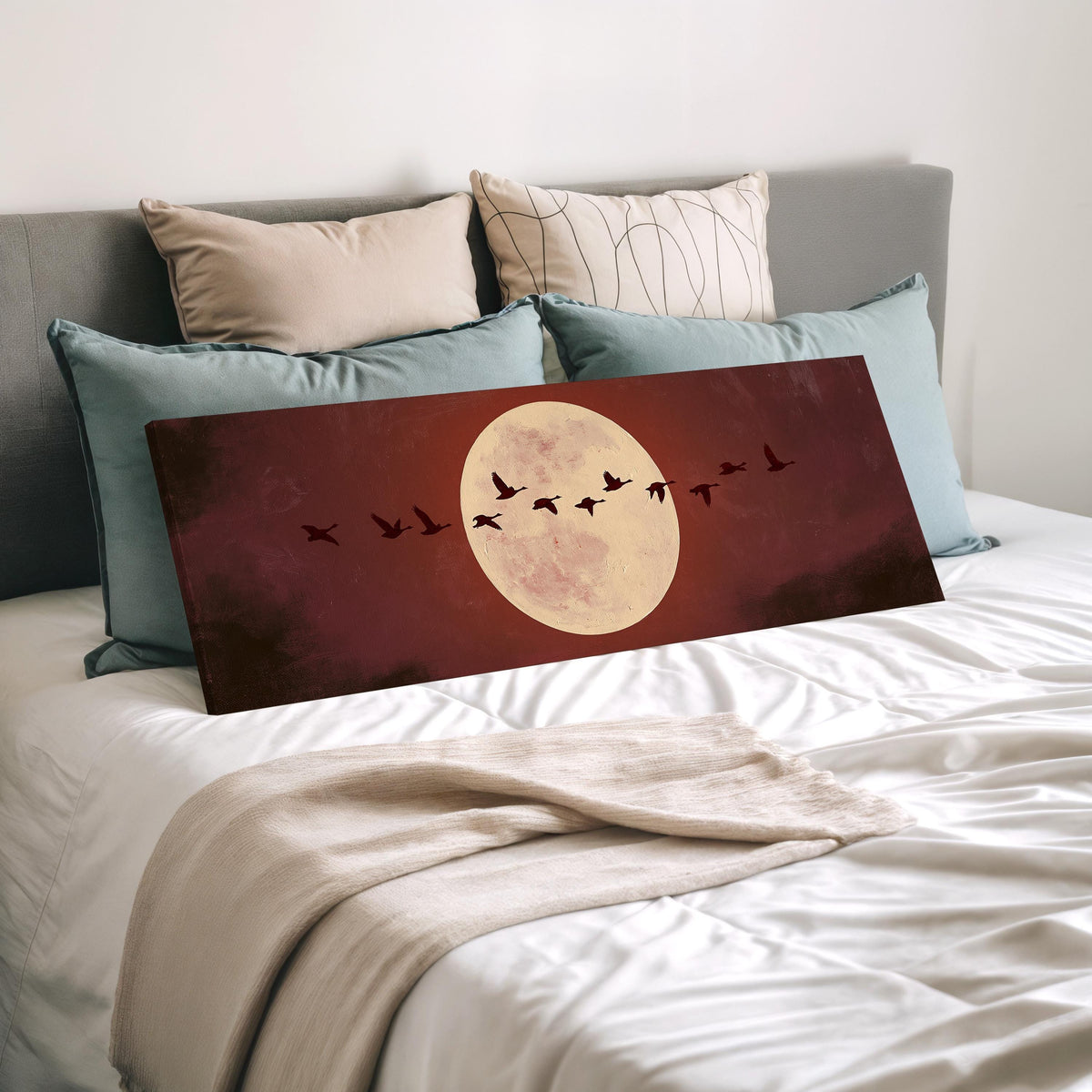 Geese crossing a pale moon on maroon wide panoramic canvas print laid on a bed to show its size
