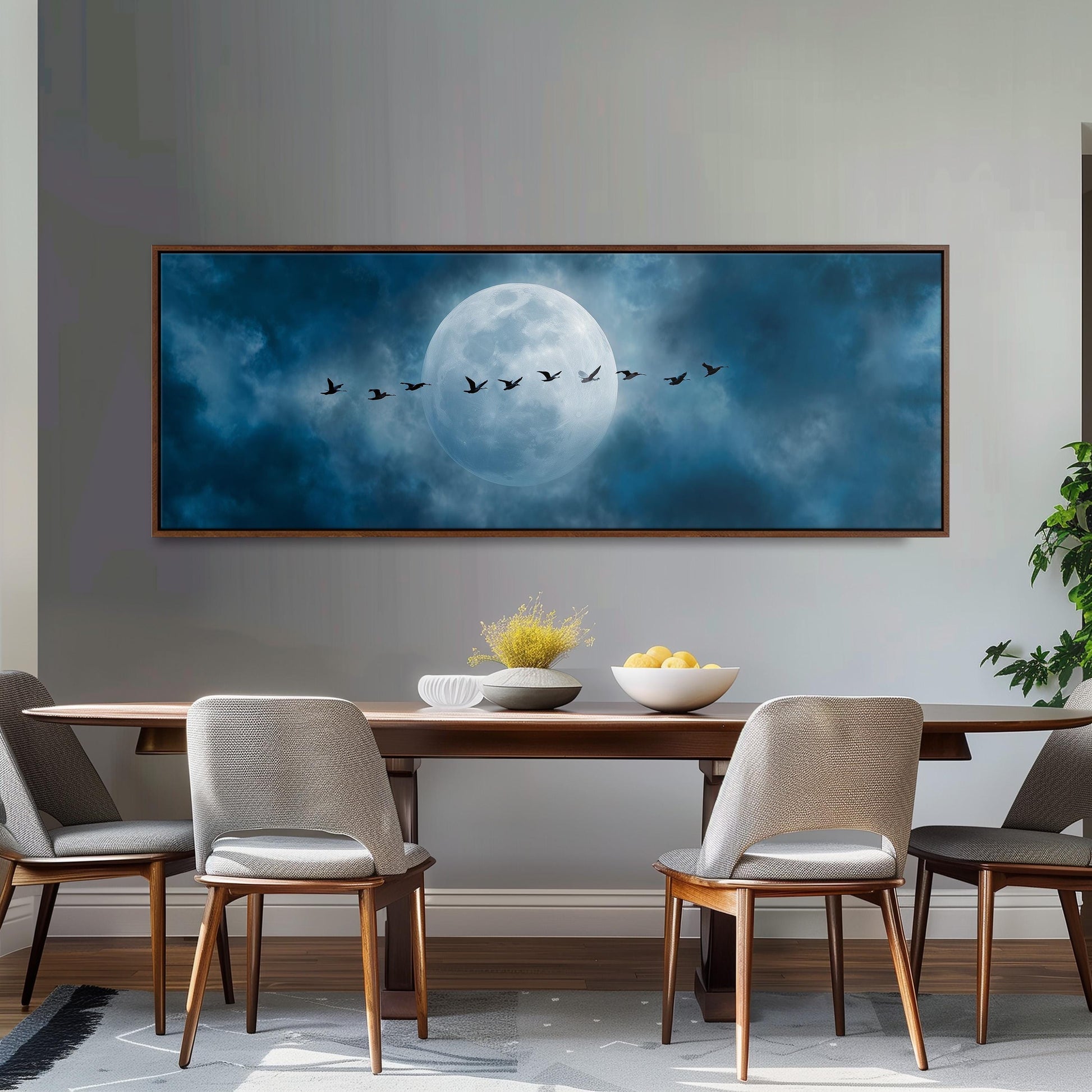 a large framed painting of a flock of birds flying across a night sky with a full moon, hanging on a wall above a wooden dining table with four chairs.