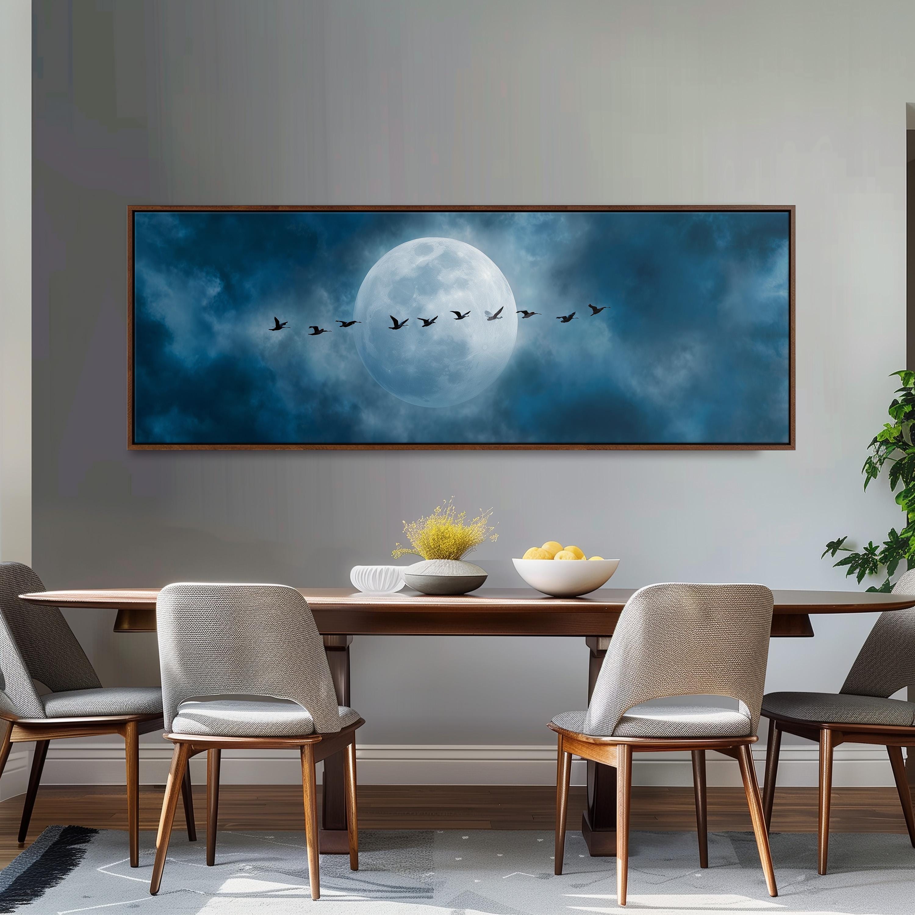 a large framed painting of a flock of birds flying across a night sky with a full moon, hanging on a wall above a wooden dining table with four chairs.