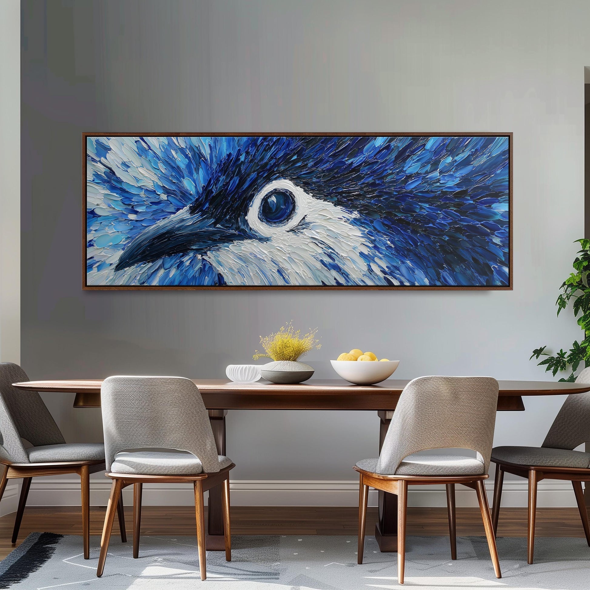 a large painting of a blue bird's eye on the wall above a wooden dining table with four chairs.
