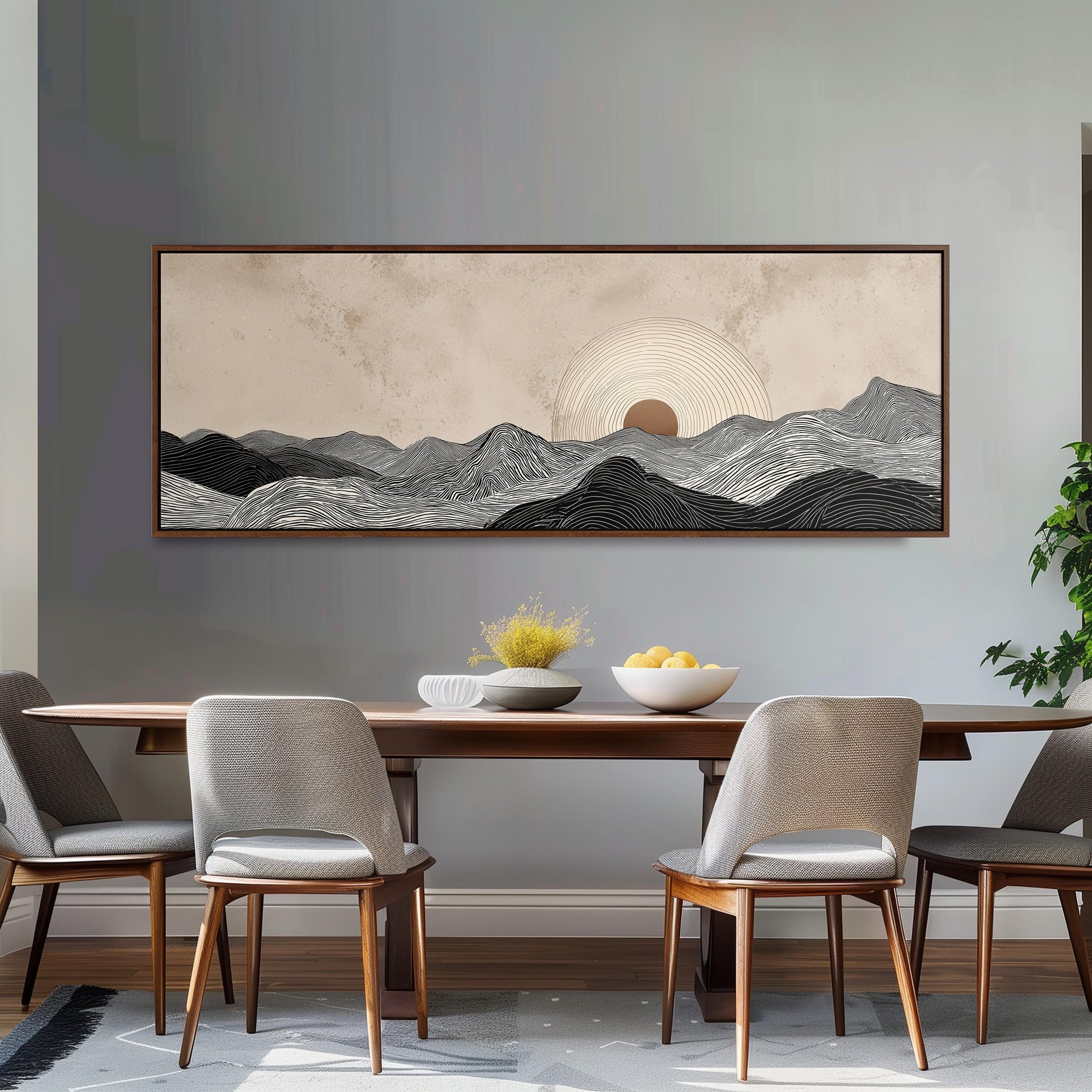 a dining room with a large, framed landscape painting hanging on the wall above a wooden dining table with four chairs. The painting depicts a serene mountain landscape with a sun rising over the horizon.