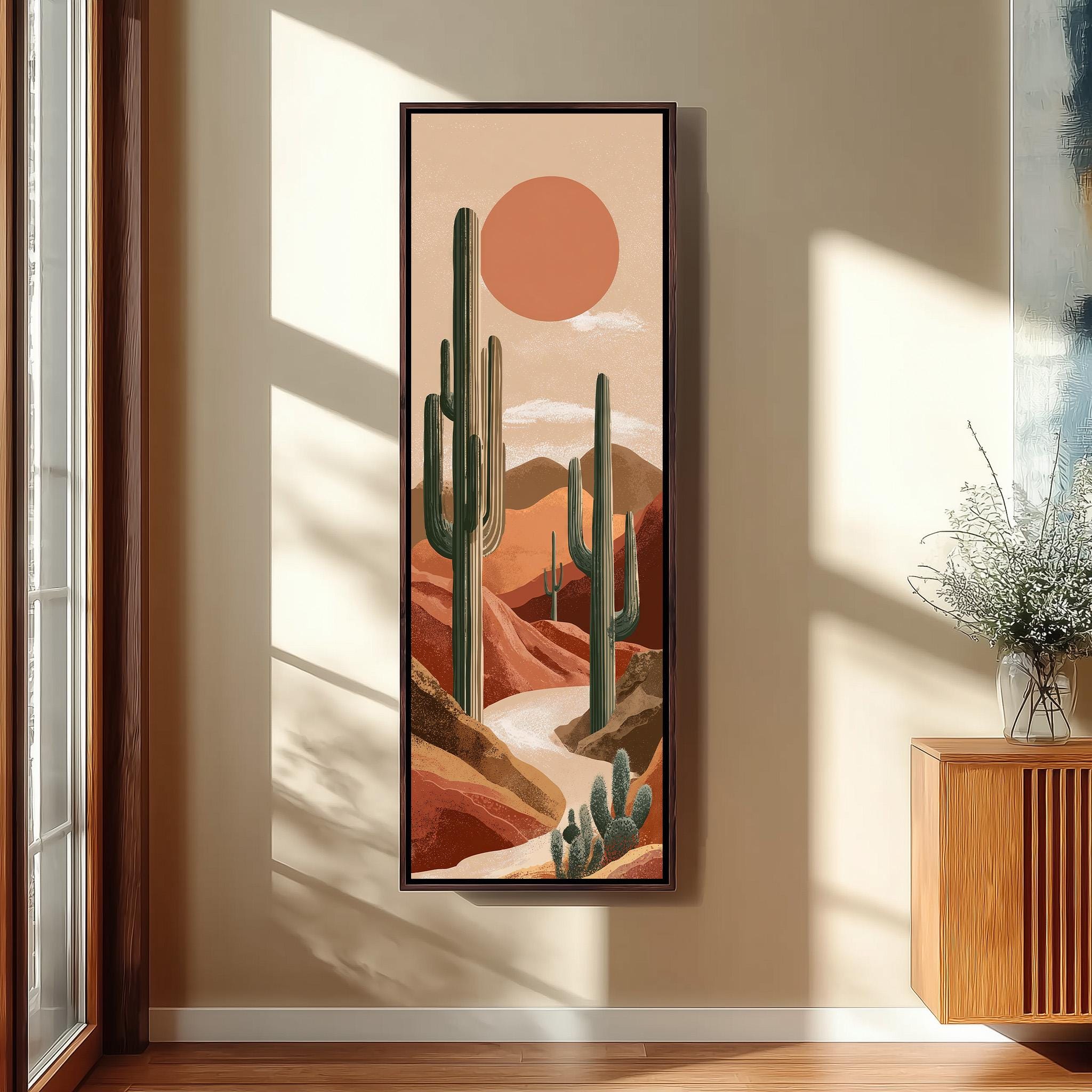 a framed painting of a desert landscape with cacti and mountains in the background, hanging on a wall.