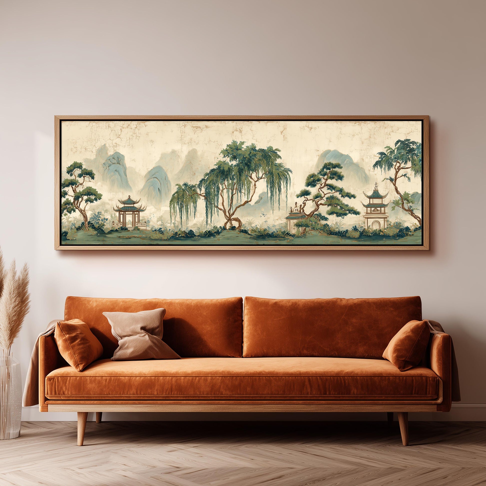 a large, framed painting of a serene landscape with mountains, trees, and pagodas hanging on a wall above a brown sofa.