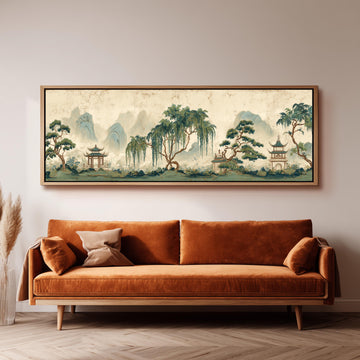 a large, framed painting of a serene landscape with mountains, trees, and pagodas hanging on a wall above a brown sofa.