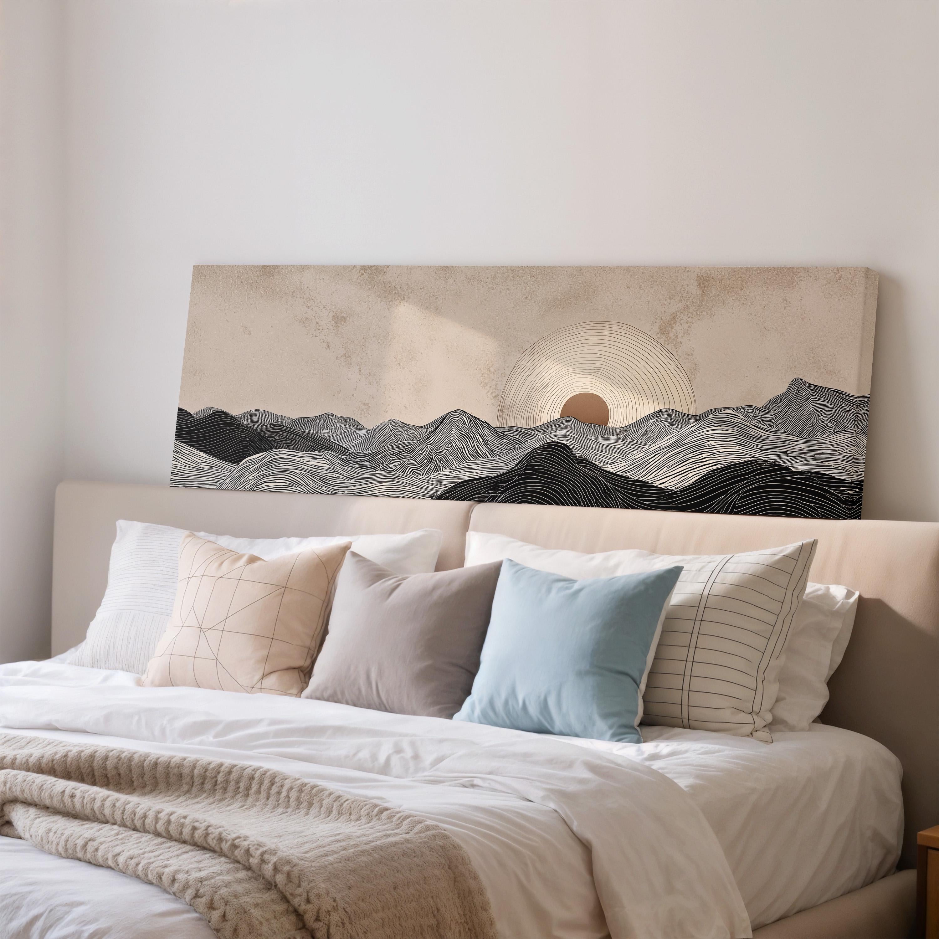a large bed with a white comforter and a variety of pillows, including a blue pillow and a striped pillow. Above the bed, there is a large canvas print depicting a mountain landscape with a sun in the background.
