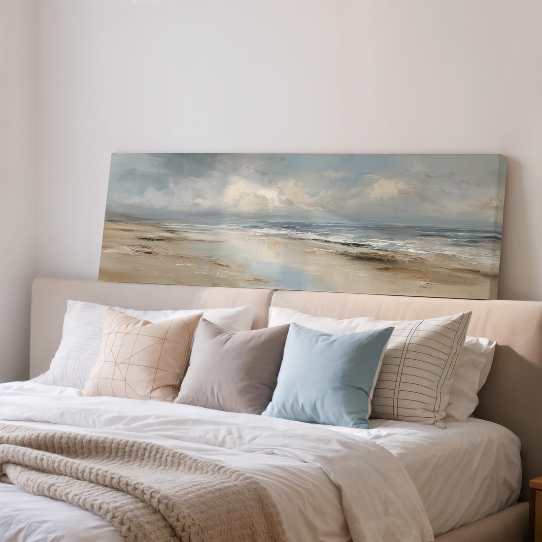 a large painting of a beach scene hanging above a bed with white bedding and various pillows.