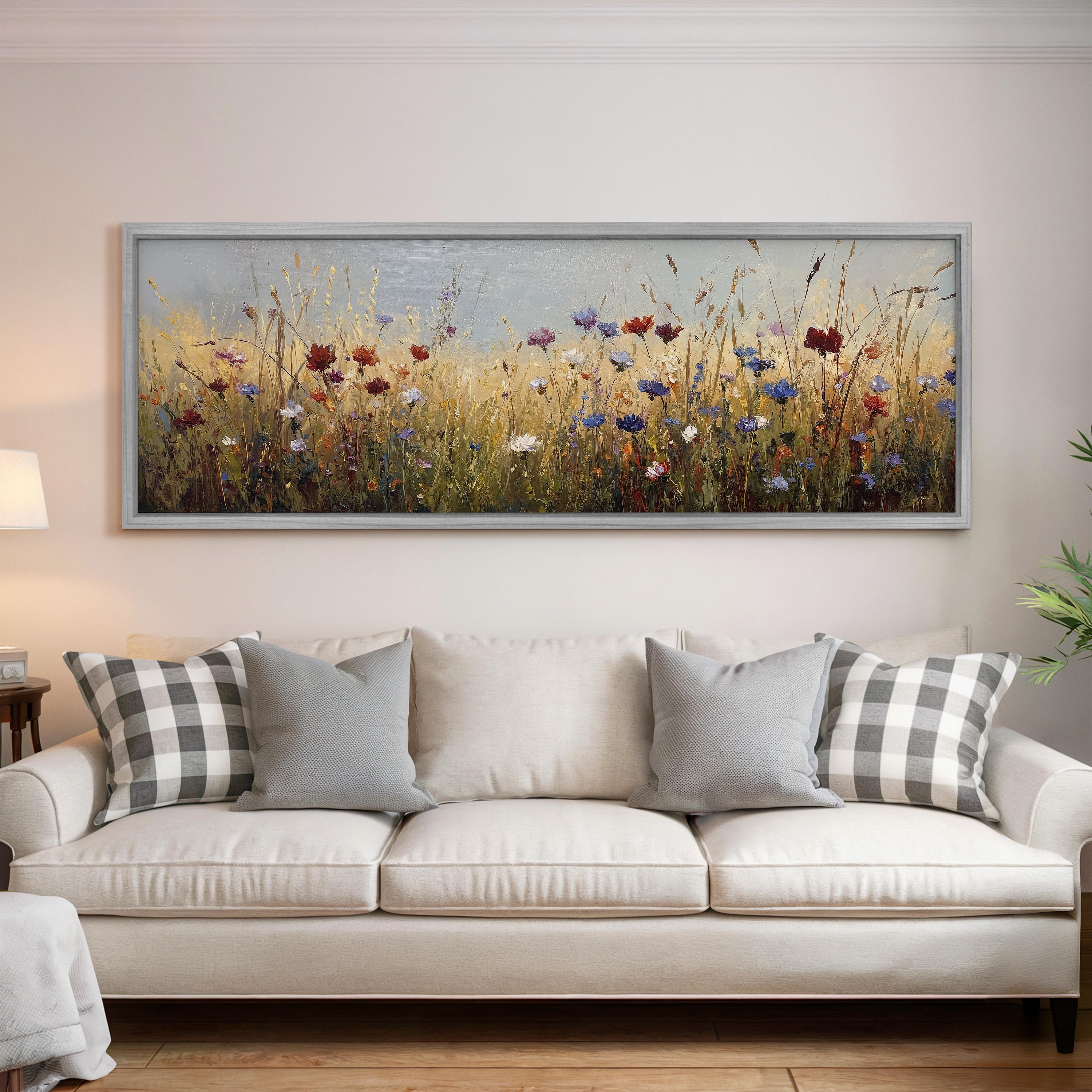 a large, framed painting of a field of flowers hanging on a wall above a white couch with gray and white plaid throw pillows.