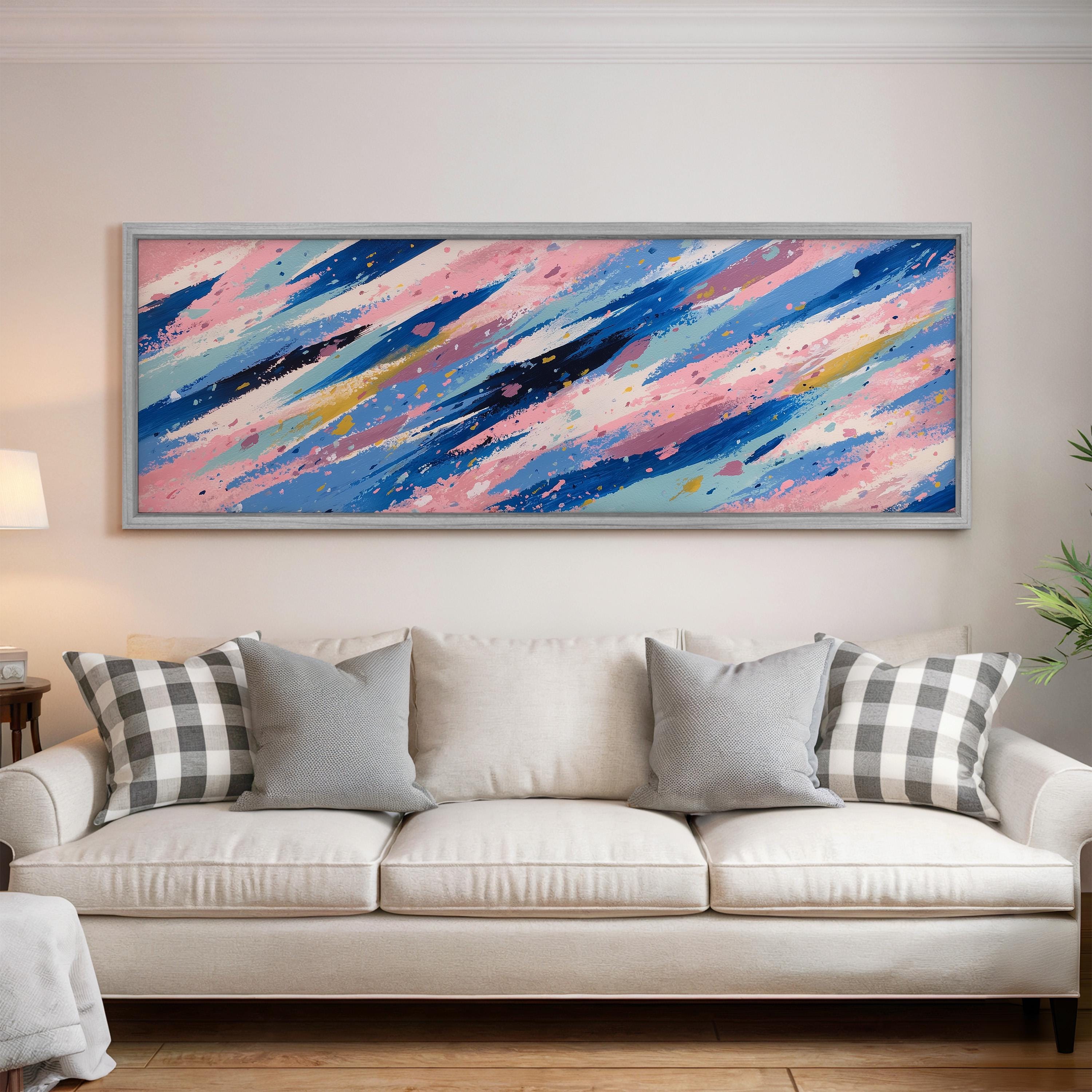 a large, colorful abstract painting hanging on a wall above a white couch with gray and black plaid throw pillows.