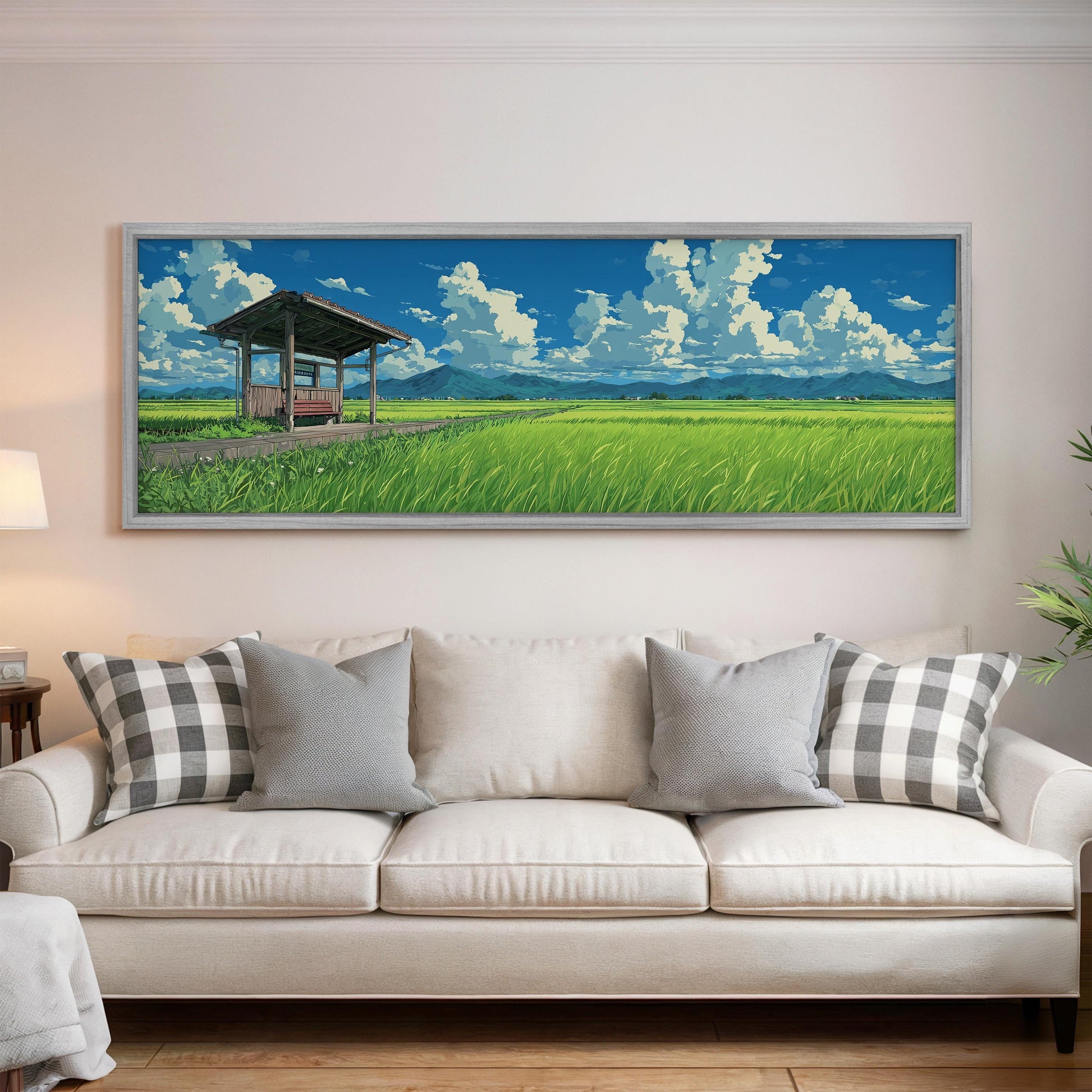 a large, framed painting of a serene landscape with a grassy field, a wooden structure, and a blue sky with white clouds. The painting is hung on a wall above a white couch with gray and white patterned pillows.