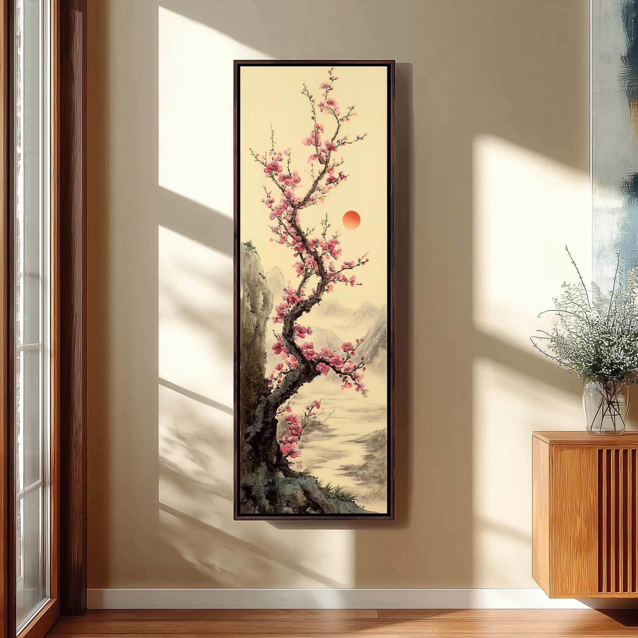 a large framed painting of a cherry blossom tree with pink flowers, hanging on a wall in a room with a wooden cabinet and a vase of flowers.