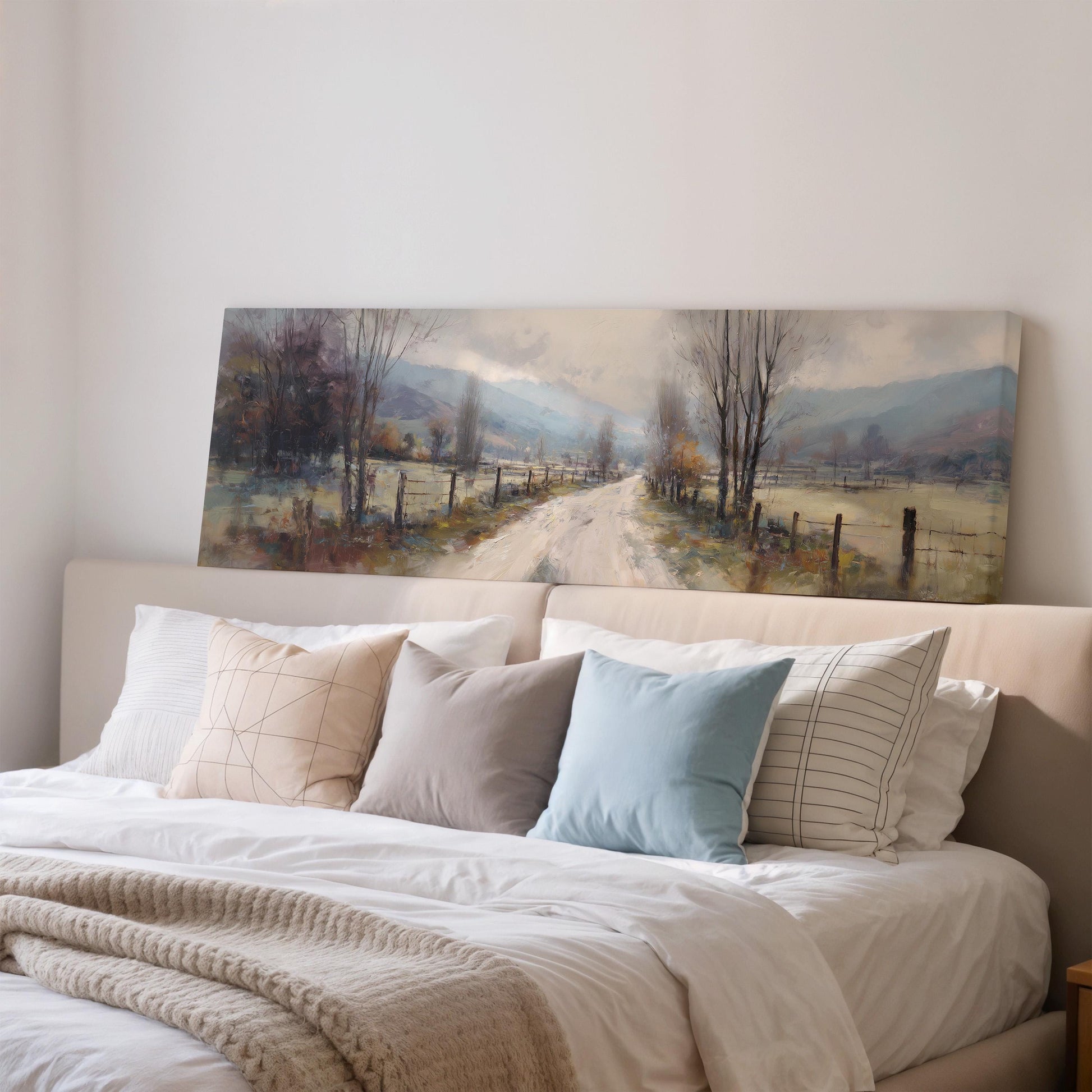 a large painting of a country road with trees and a fence, hanging above a bed with white bedding and pillows.