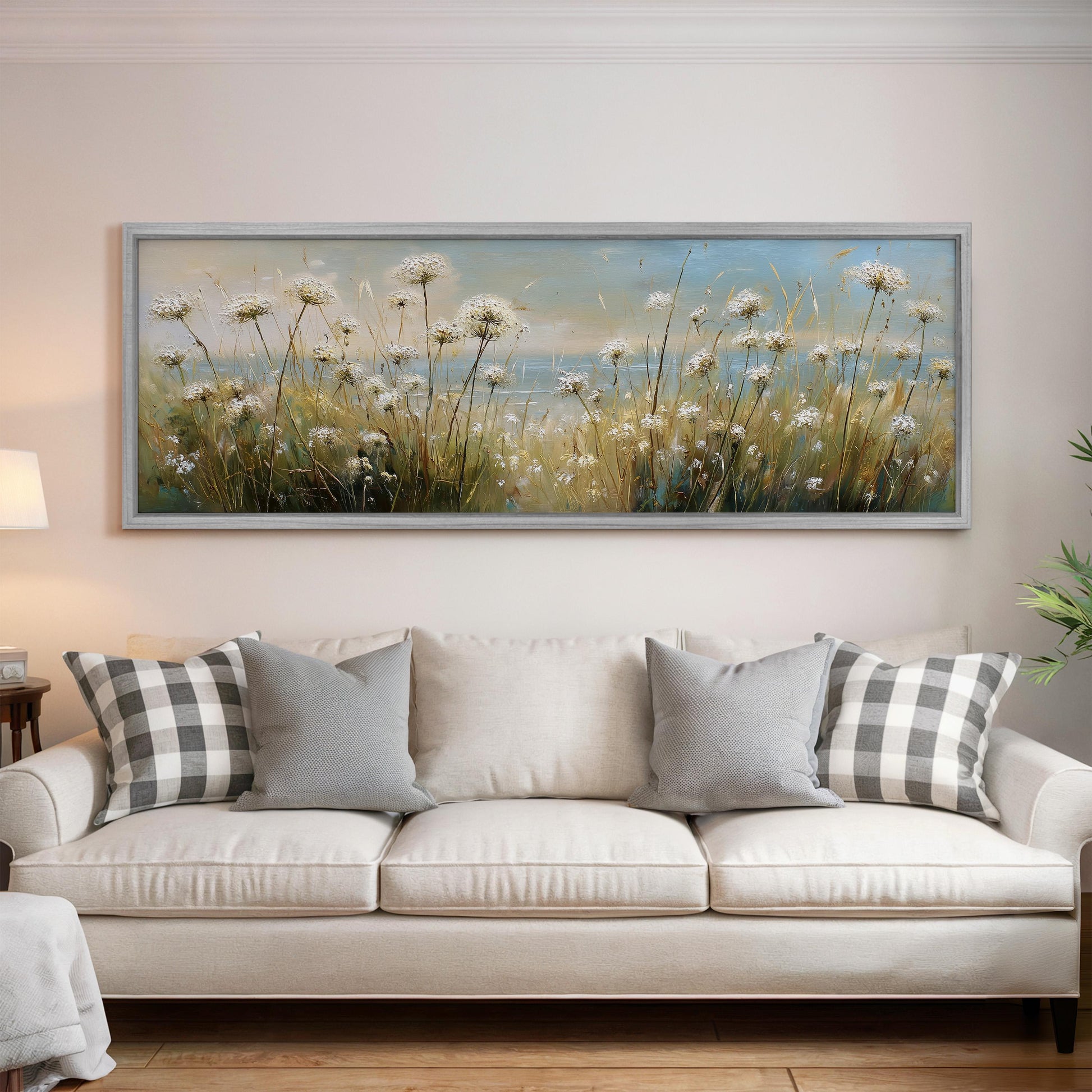 a large painting of a field of flowers hanging on a wall above a white sofa with gray and white pillows.