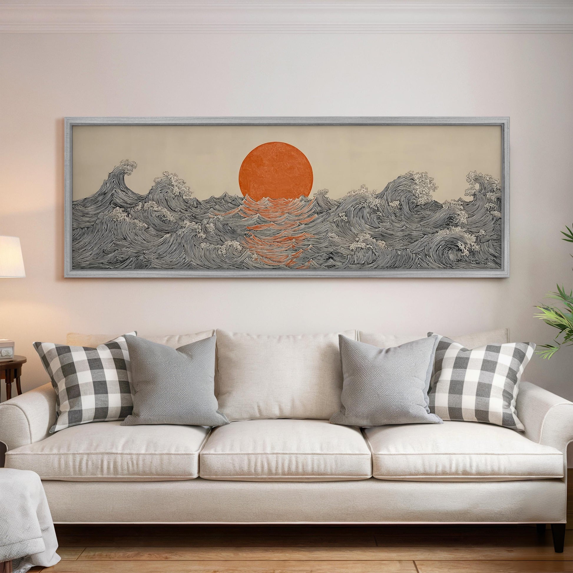 a large, framed artwork depicting a sunset over a wave-filled ocean, hanging on a wall above a white couch with patterned throw pillows.