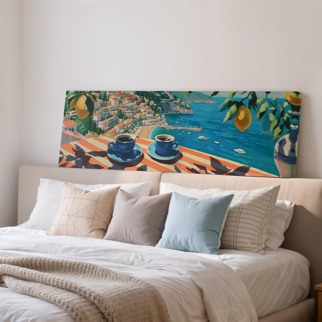 a large painting of a coastal town with a view of the sea, hanging on a wall above a brown sofa with two pillows.