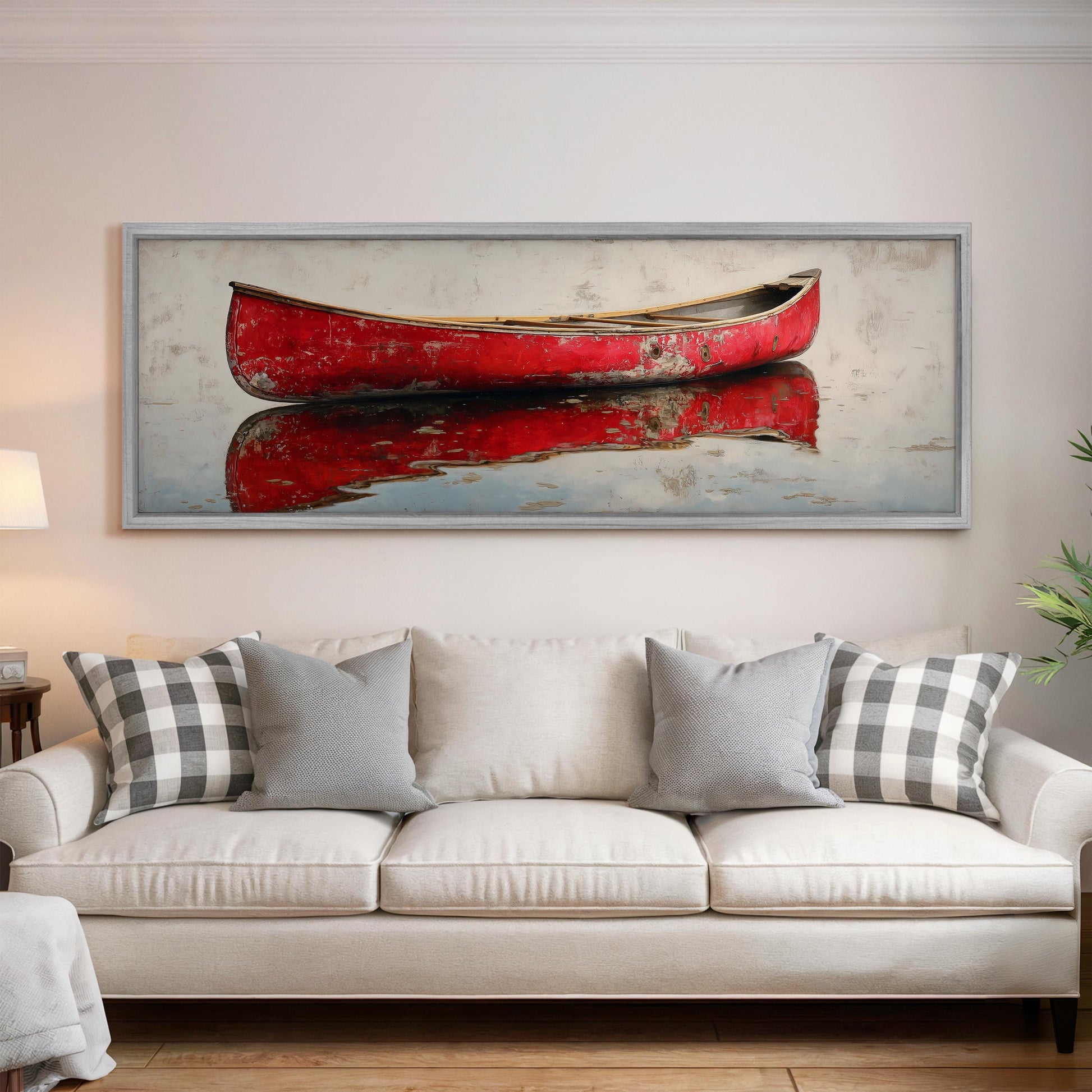 a large, framed painting of a red canoe on a white wall above a white couch with gray and white plaid throw pillows.