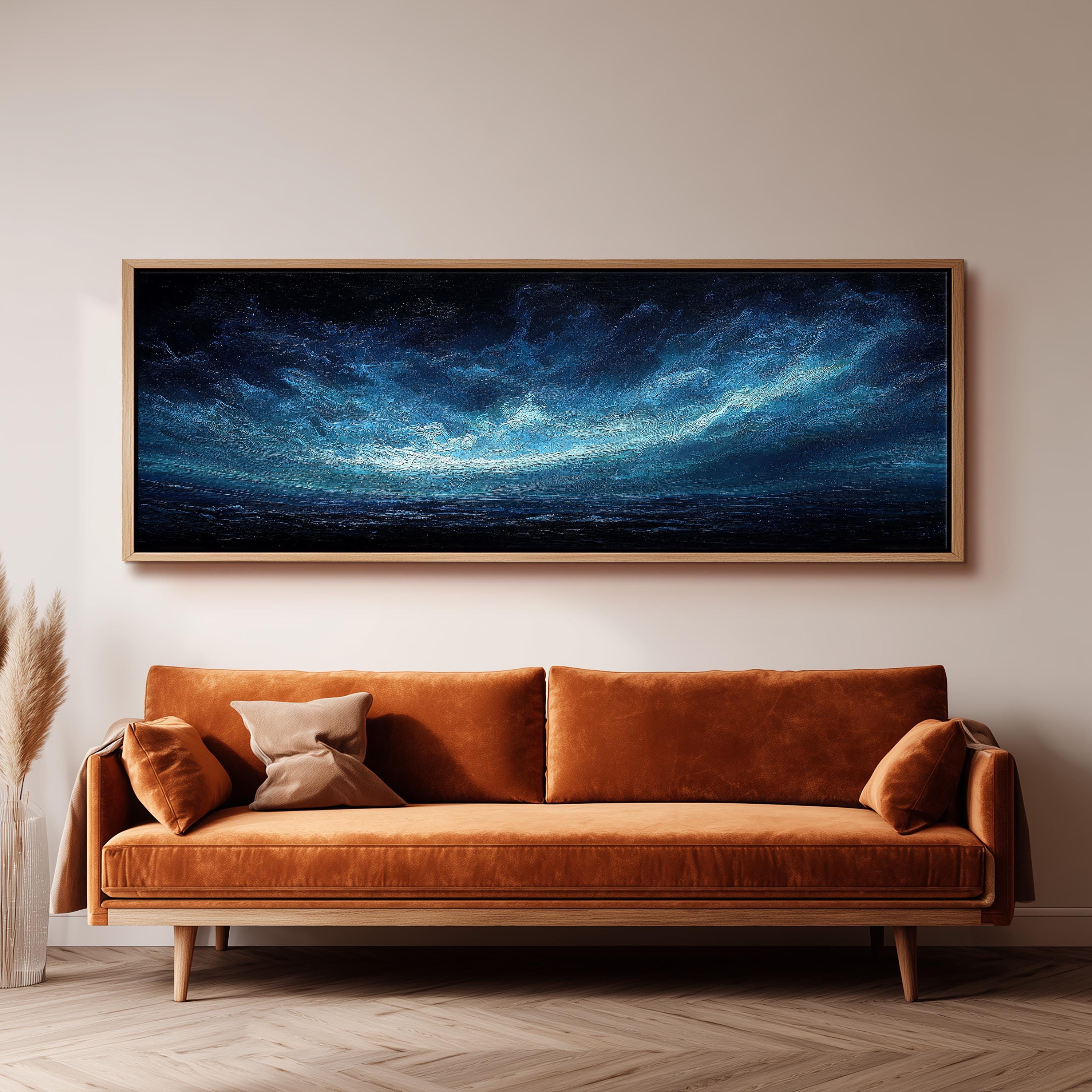 a large, framed painting of a night sky with a dark blue background and a bright, white, wispy cloud formation. The painting is hanging on a wall above a brown, plush couch with orange cushions.