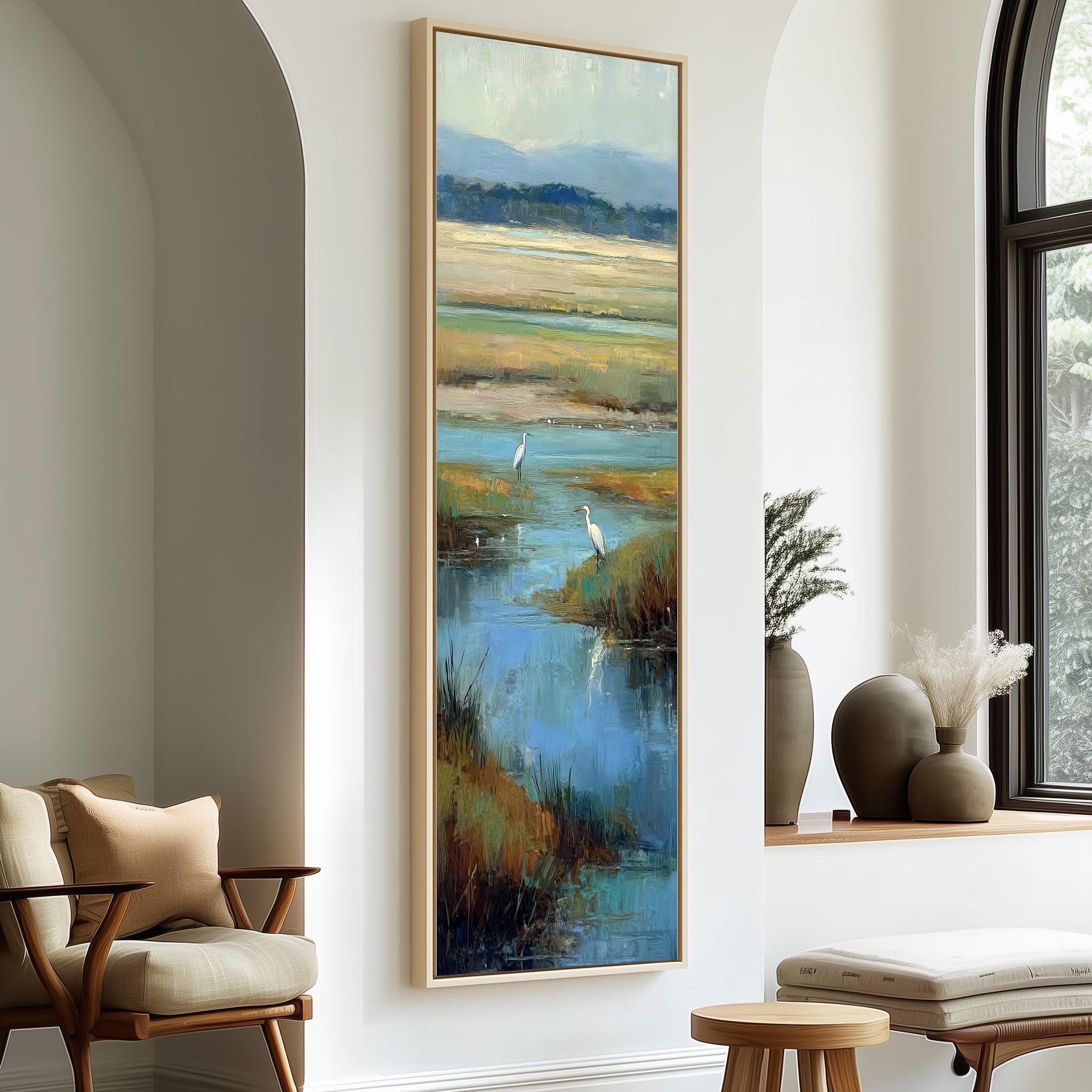 a large painting of a serene landscape with two white birds standing in a body of water, surrounded by lush greenery. The painting is hung on a white wall, and there are two chairs and a small table in the foreground.