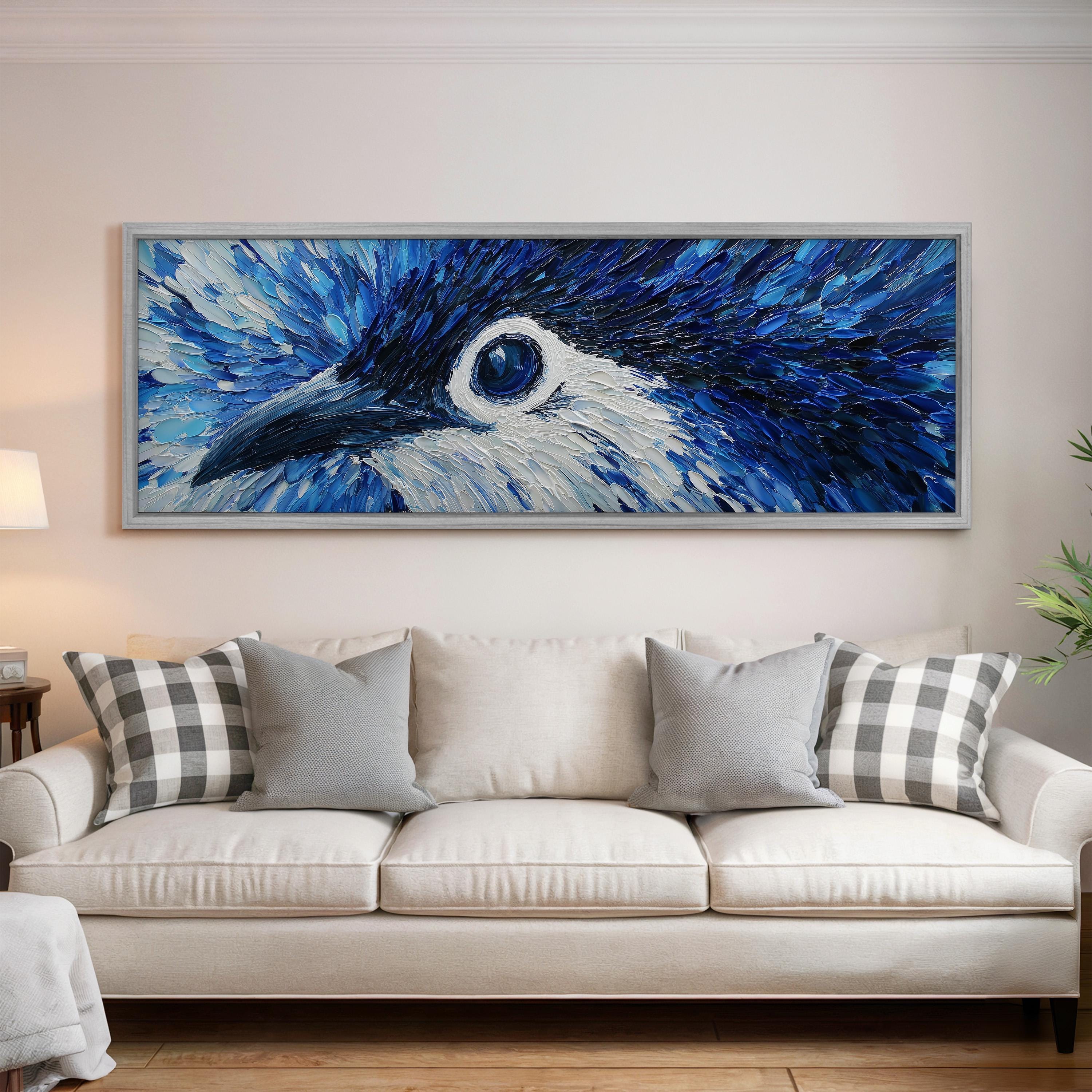 a large, framed painting of a blue bird's eye on the wall above a white couch with gray and white plaid throw pillows.