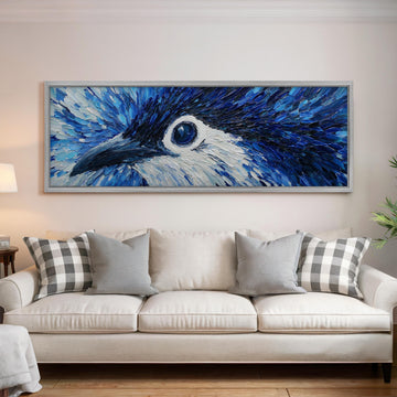 a large, framed painting of a blue bird's eye on the wall above a white couch with gray and white plaid throw pillows.