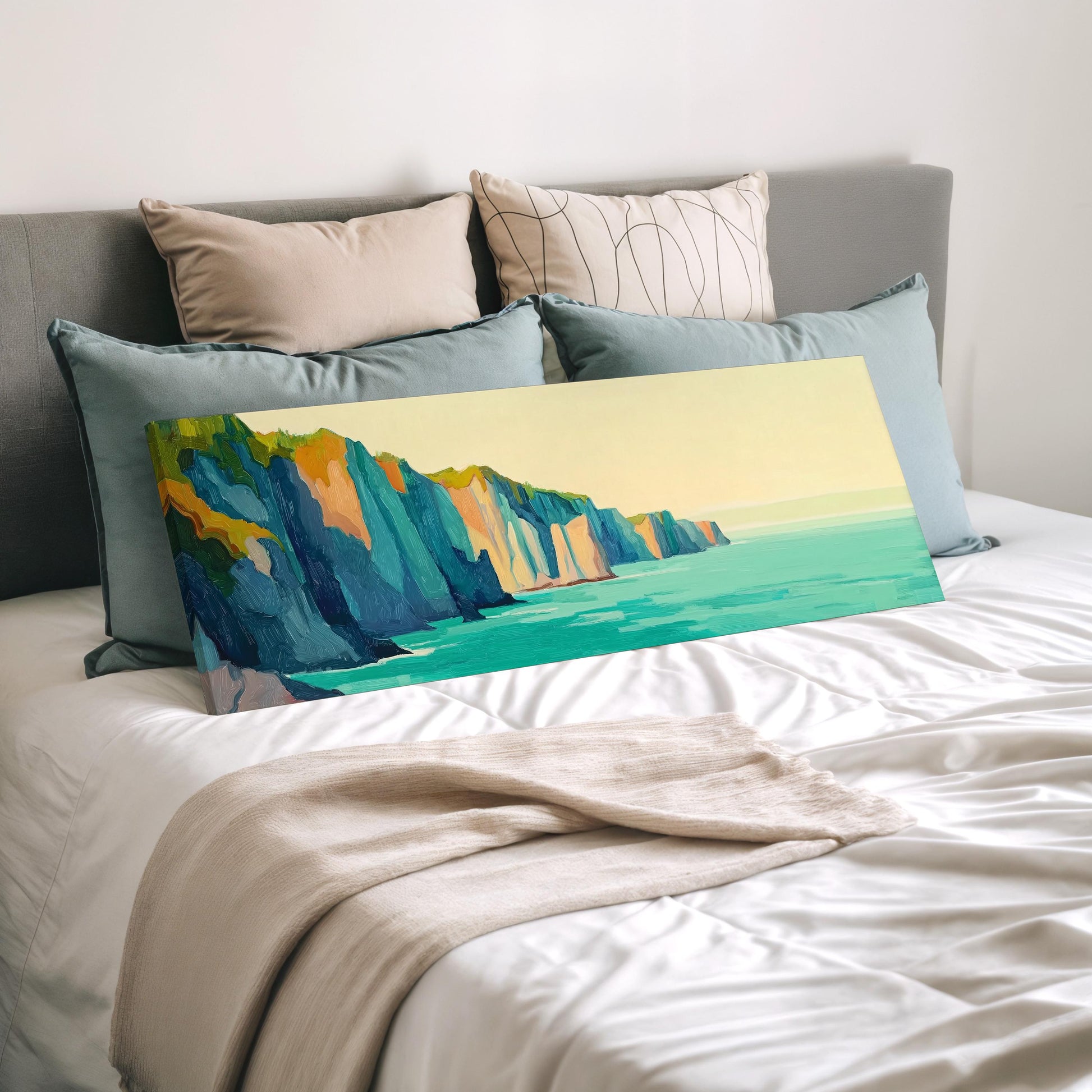 a large painting of a cliff overlooking the ocean, displayed on a bed with a white comforter and pillows.