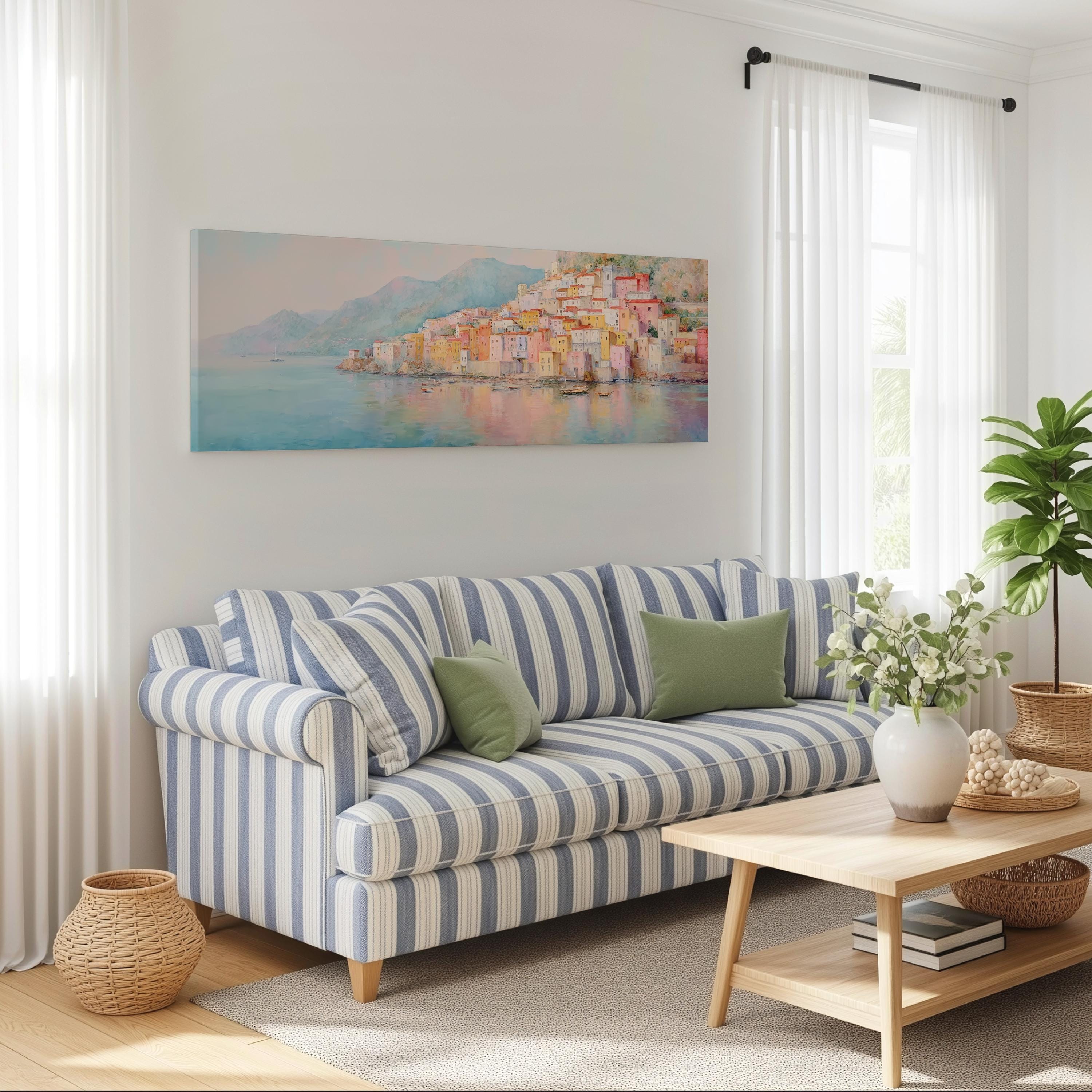 a cozy living room with a striped blue and white sofa, a wooden coffee table, and a large window with white curtains. Above the sofa, there is a framed painting of a coastal town.