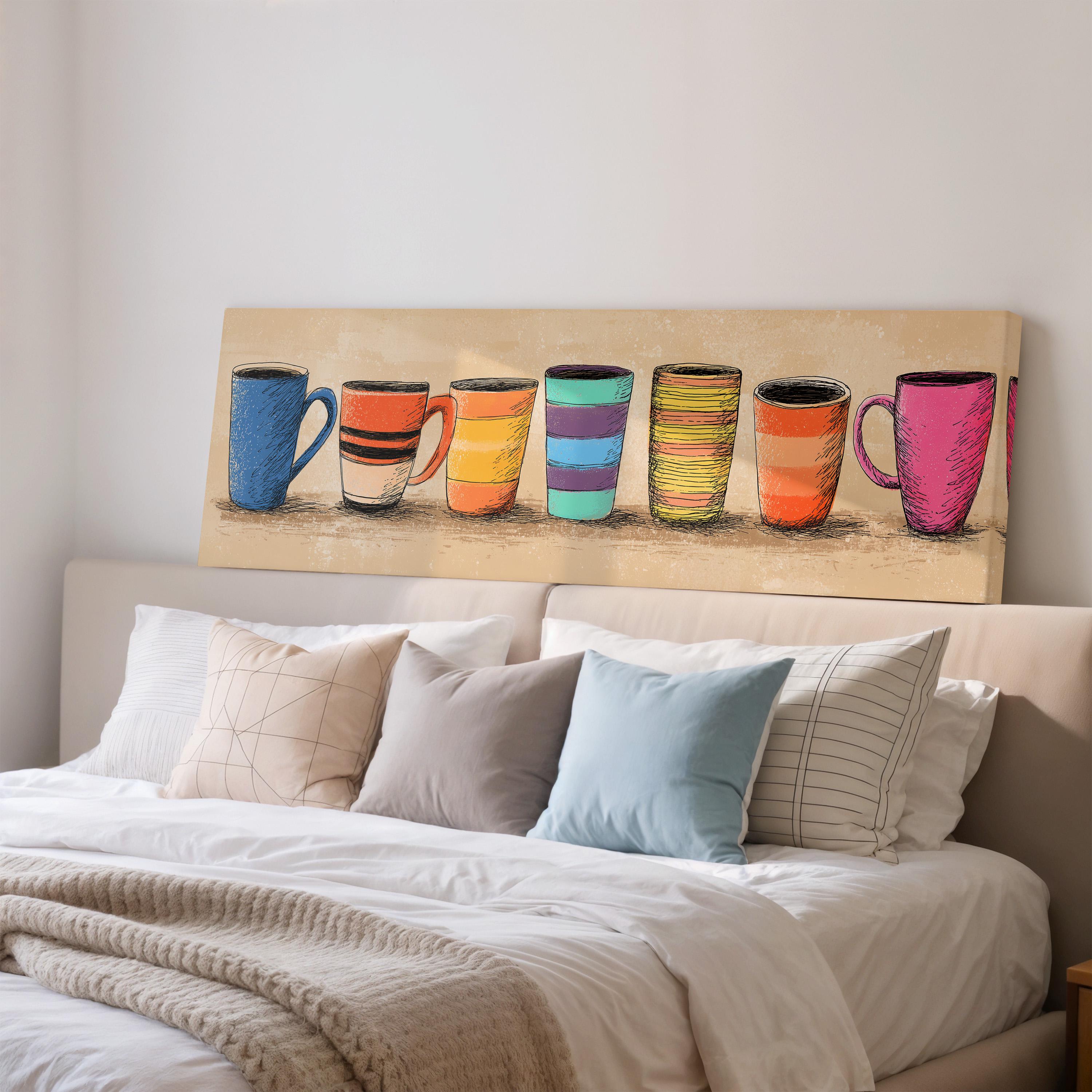 a cozy bedroom scene with a bed adorned with white sheets and a variety of colorful pillows. Above the bed, there is a large canvas print depicting a row of colorful mugs or cups, adding a unique and artistic touch to the room.
