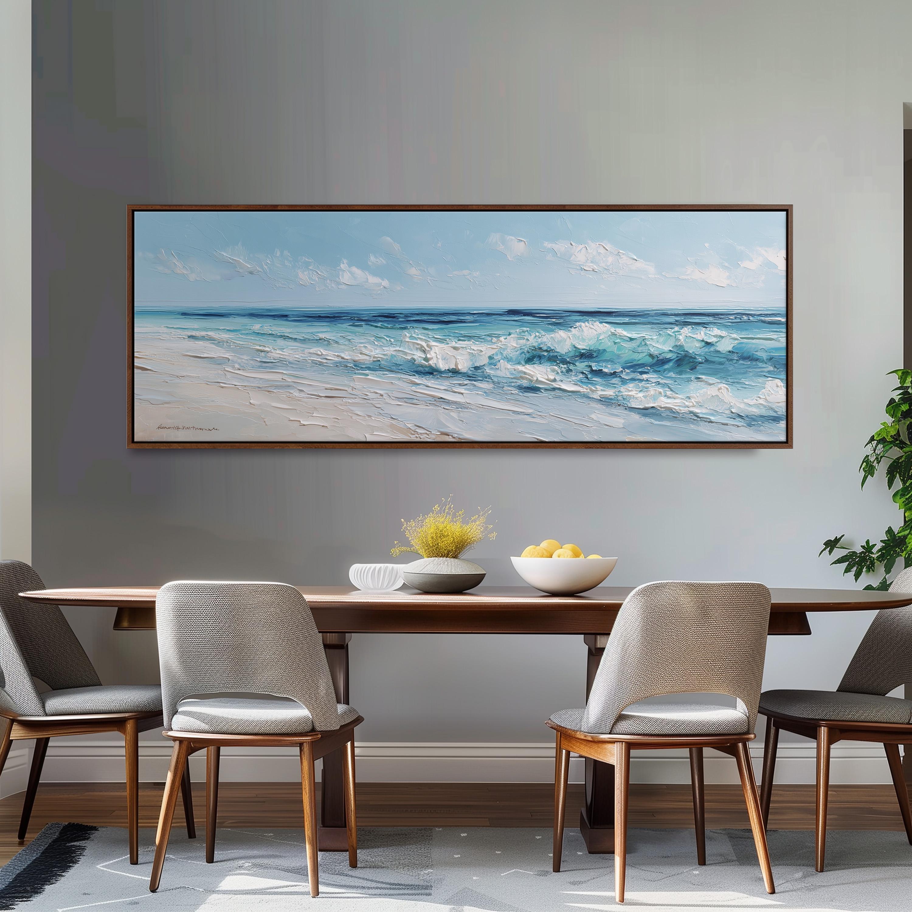 a large painting of a beach scene hanging on a wall above a wooden dining table with four chairs. The painting depicts a serene beach landscape with waves crashing on the shore and a clear blue sky above.