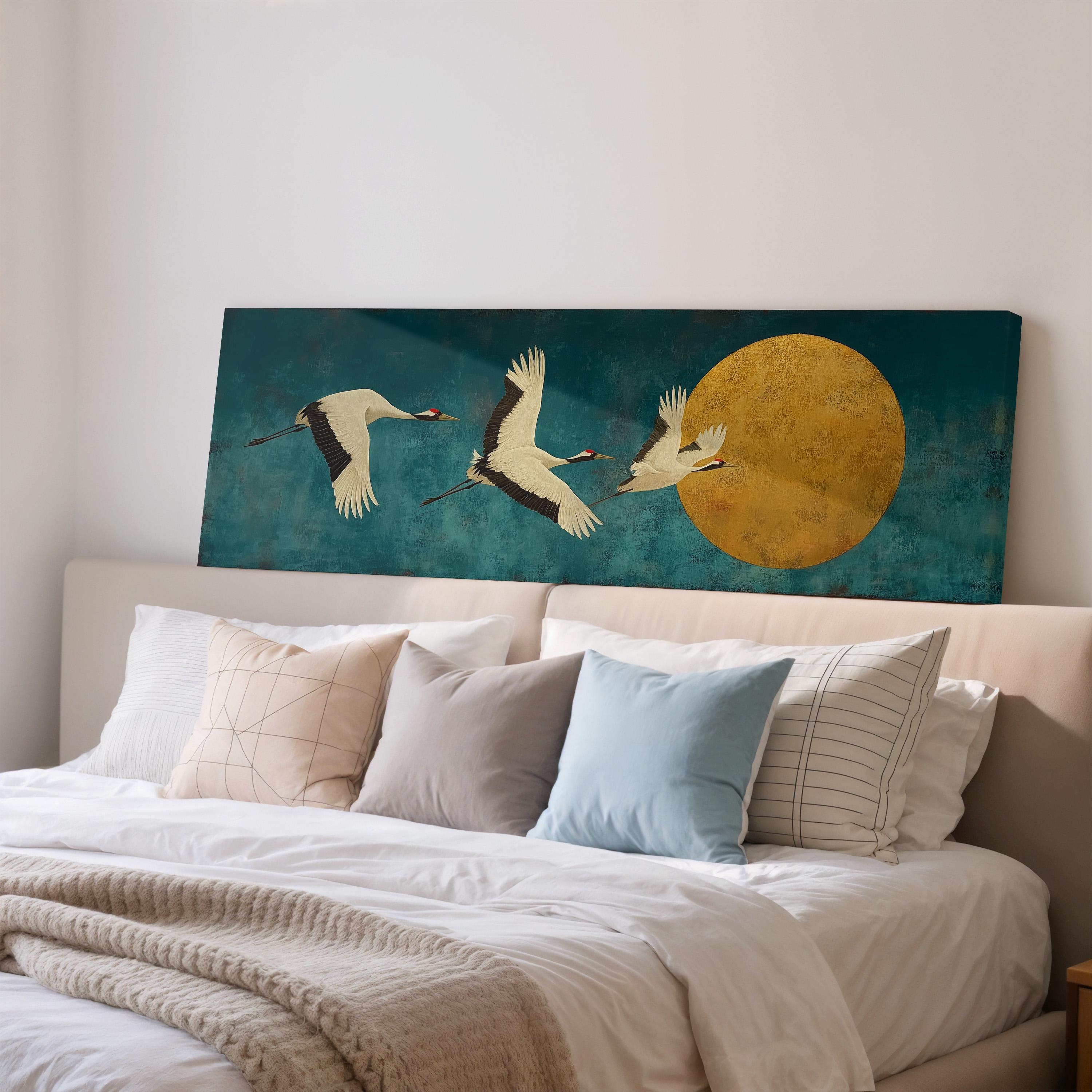 a large painting of three white birds in flight against a blue background, with a large yellow circle in the center. The painting is mounted on a wall above a bed with white pillows and a gray blanket.