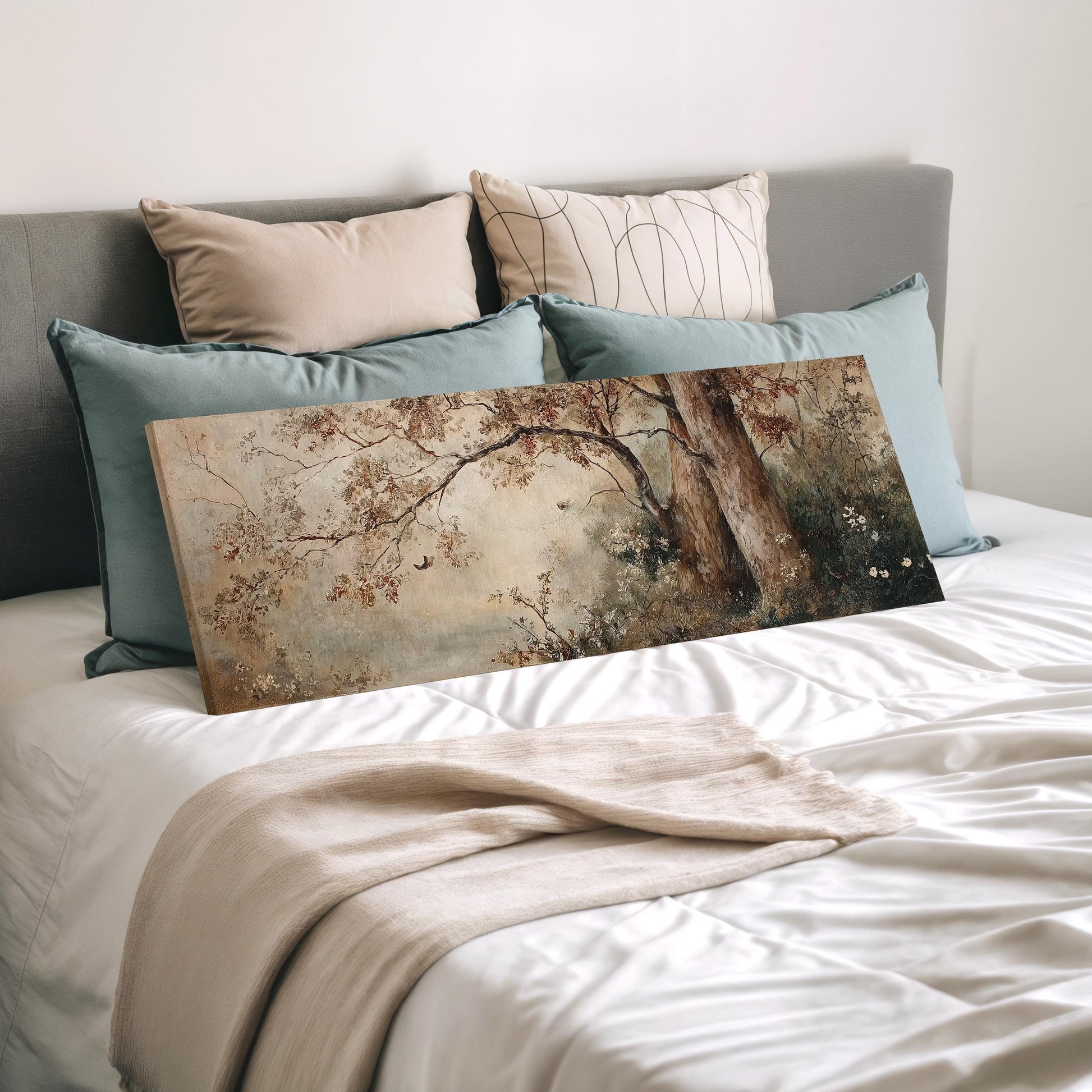 a bedroom with a bed covered in white sheets and a painting of a tree on the bed. The painting is placed on a pillow, and there are several pillows surrounding it.