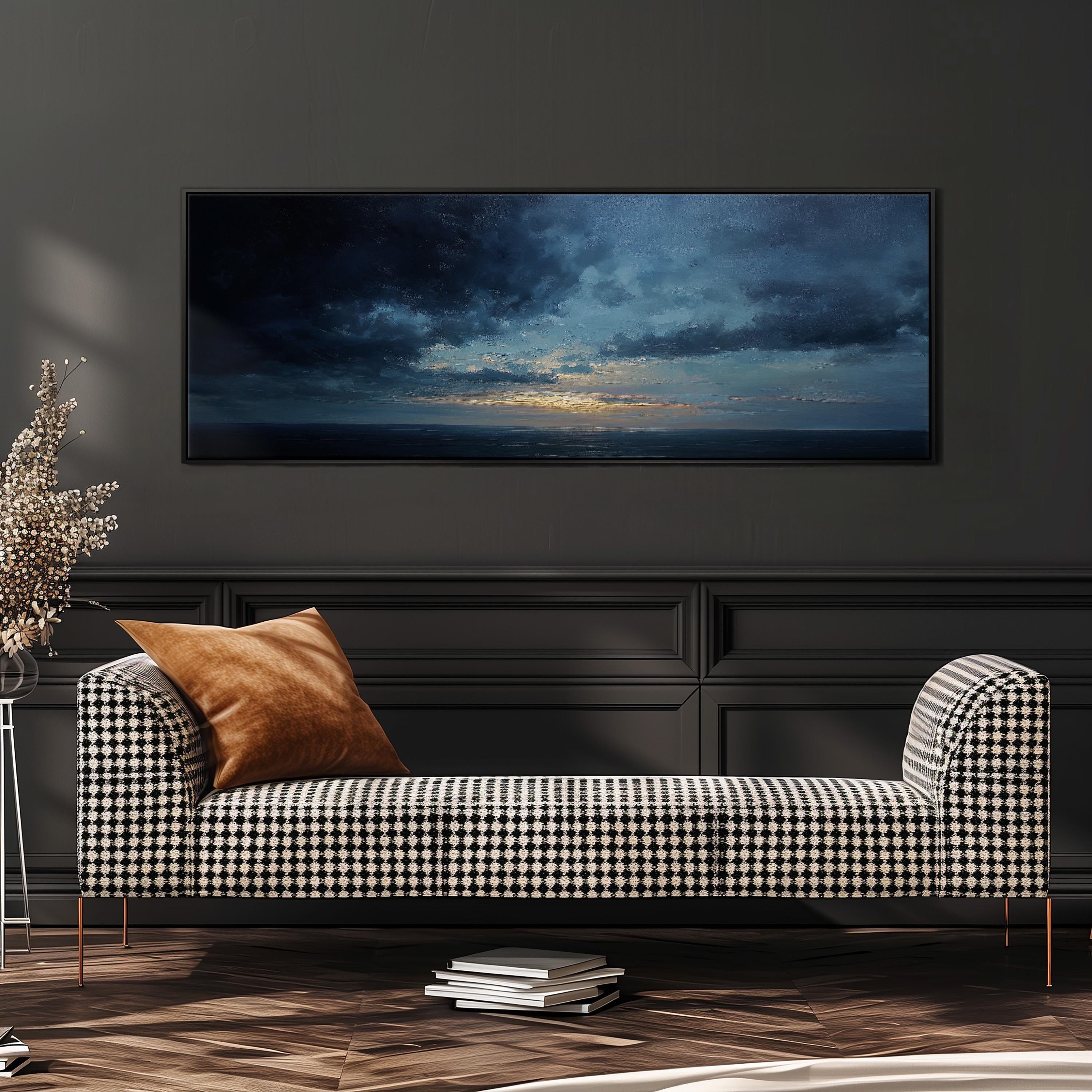 a modern living room with a black and white checkered sofa, a large framed painting of a stormy sky above the sofa, and a stack of books on the floor.