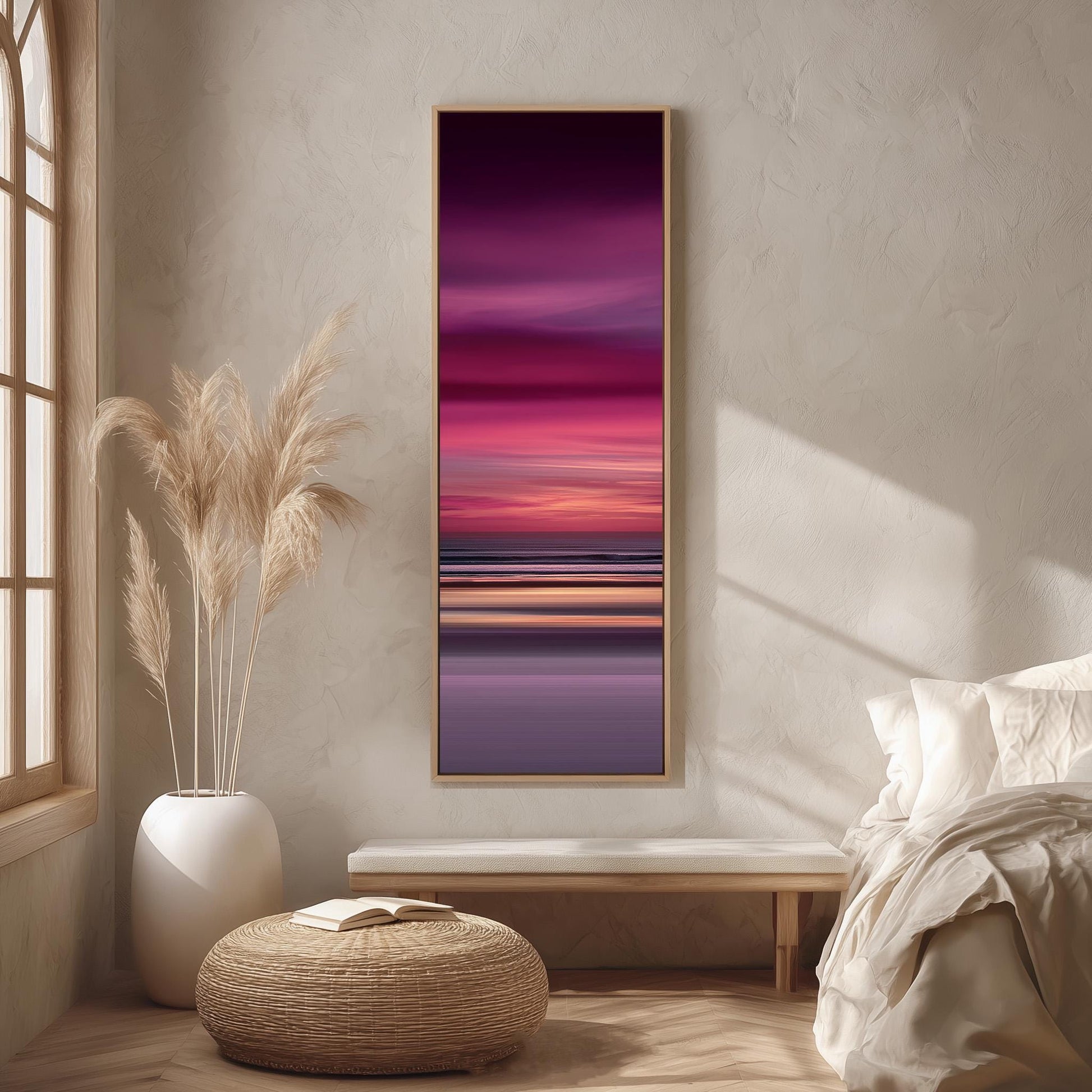 a serene bedroom scene with a large window, a bed with white linens, a woven ottoman, and a framed painting of a sunset over the ocean.