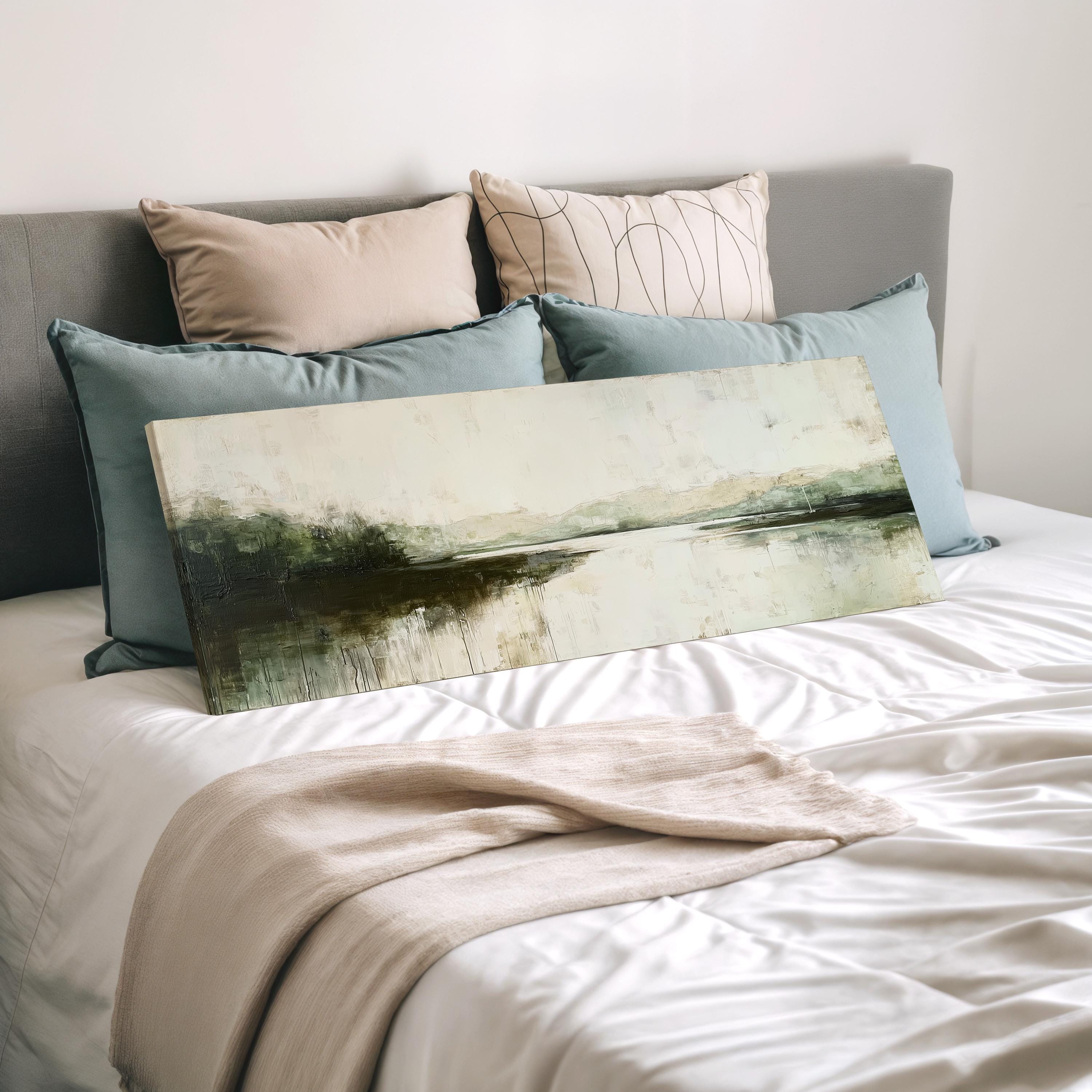 a bedroom with a bed covered in white sheets and a painting of a landscape resting on top of the bed.