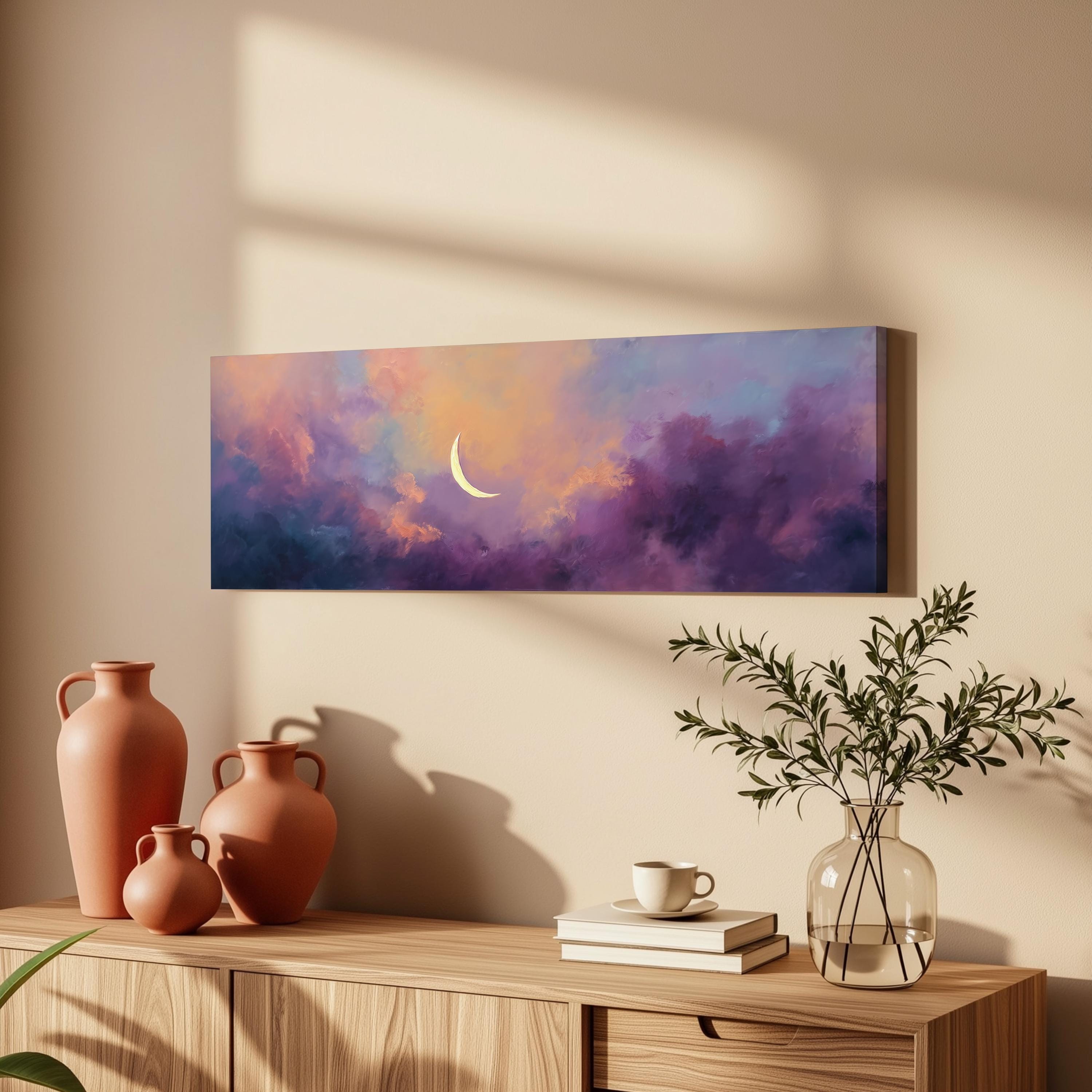 a wooden cabinet with a vase of greenery, a stack of books, and a painting of a crescent moon against a colorful sky.