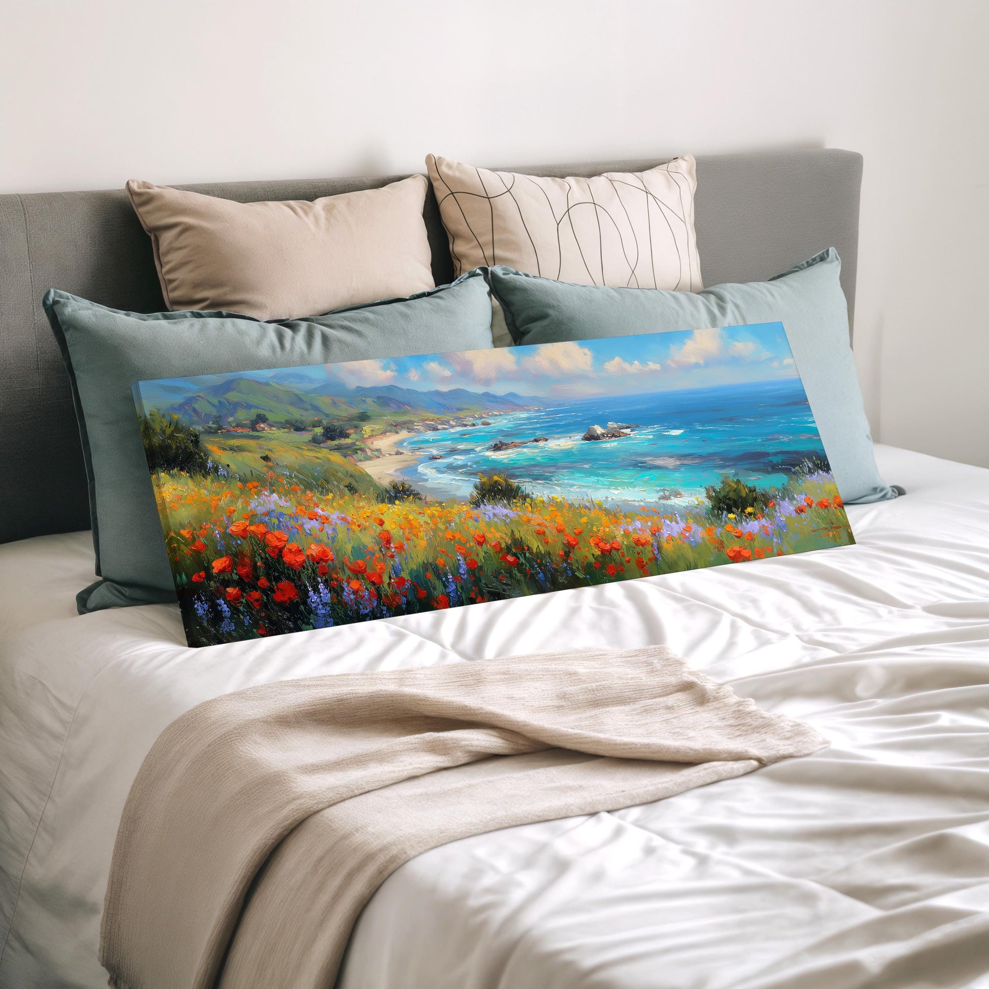 a large painting of a coastal landscape with a beach, mountains, and a blue ocean, displayed on a bed with a white comforter and pillows.