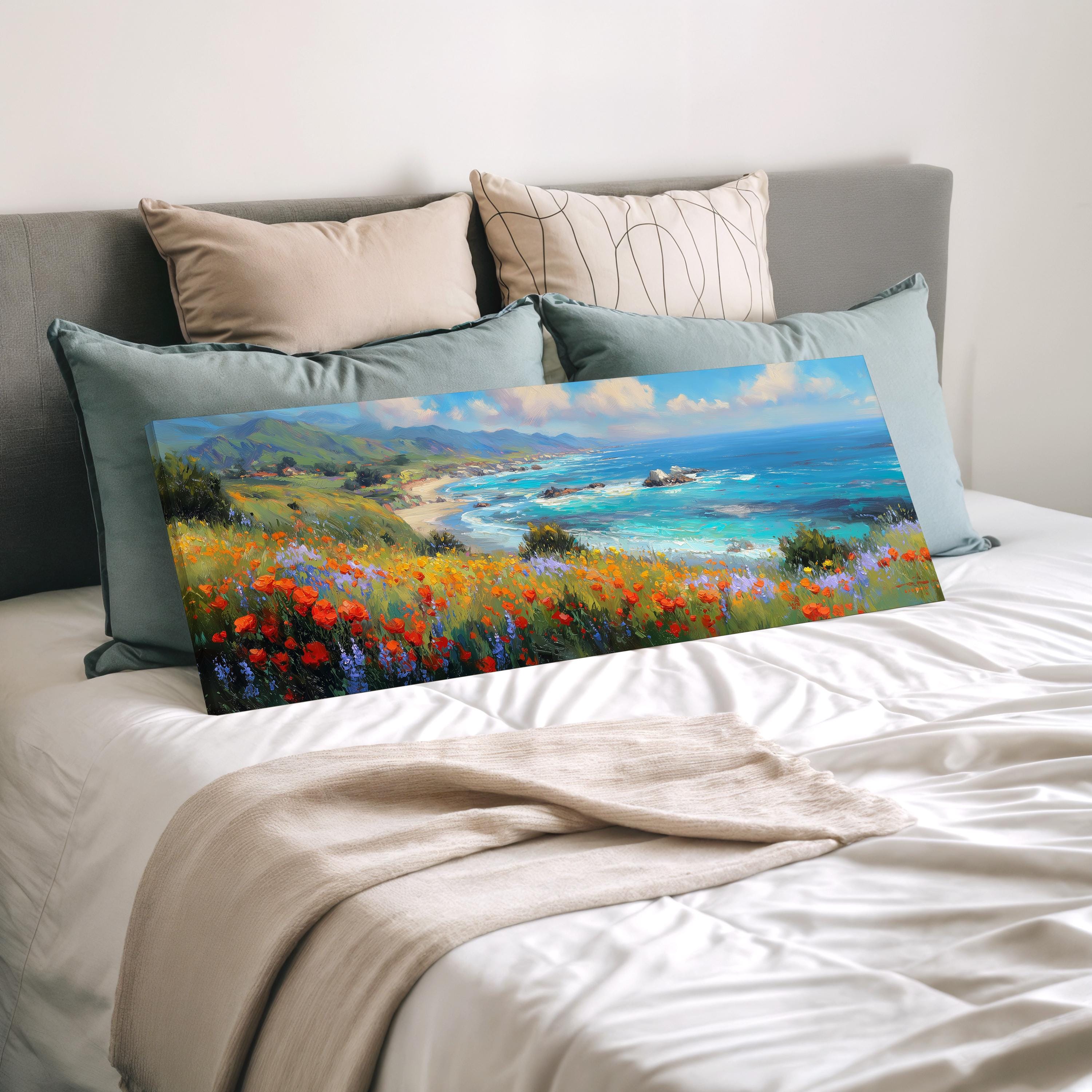 a large painting of a coastal landscape with a beach, mountains, and a blue ocean, displayed on a bed with a white comforter and pillows.