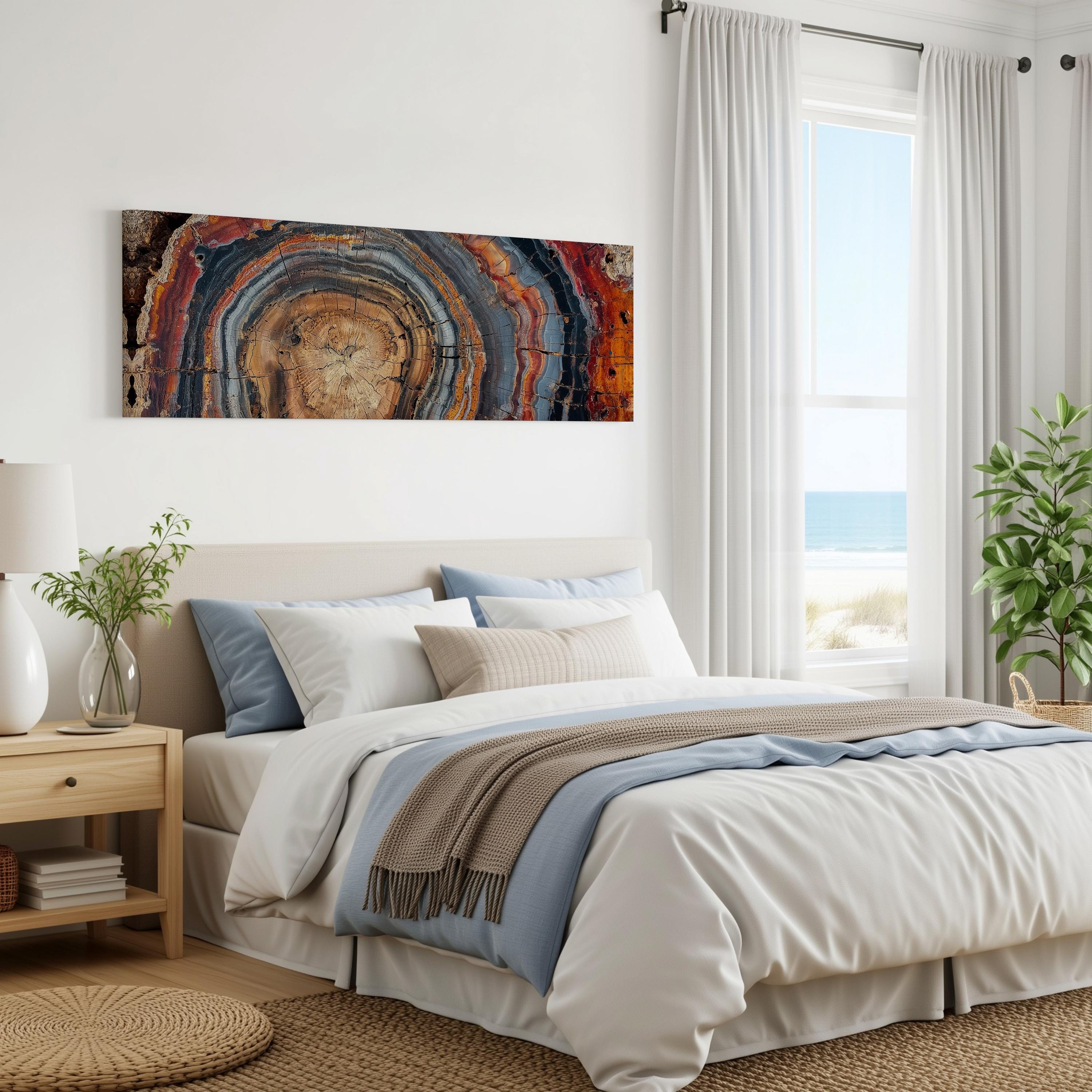 a serene bedroom with a large bed, a nightstand, and a painting on the wall. The painting features a colorful abstract design with concentric circles in various shades of blue, orange, and brown. The room has a beach view through a window, and there are potted plants and a rug on the floor, creating a cozy and inviting atmosphere.