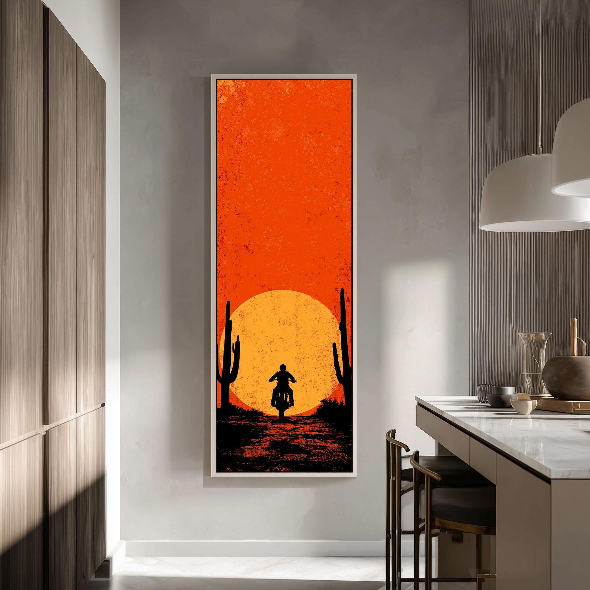 a large framed artwork depicting a person riding a motorcycle on a desert road, with a cactus in the background and a large orange sun in the sky.