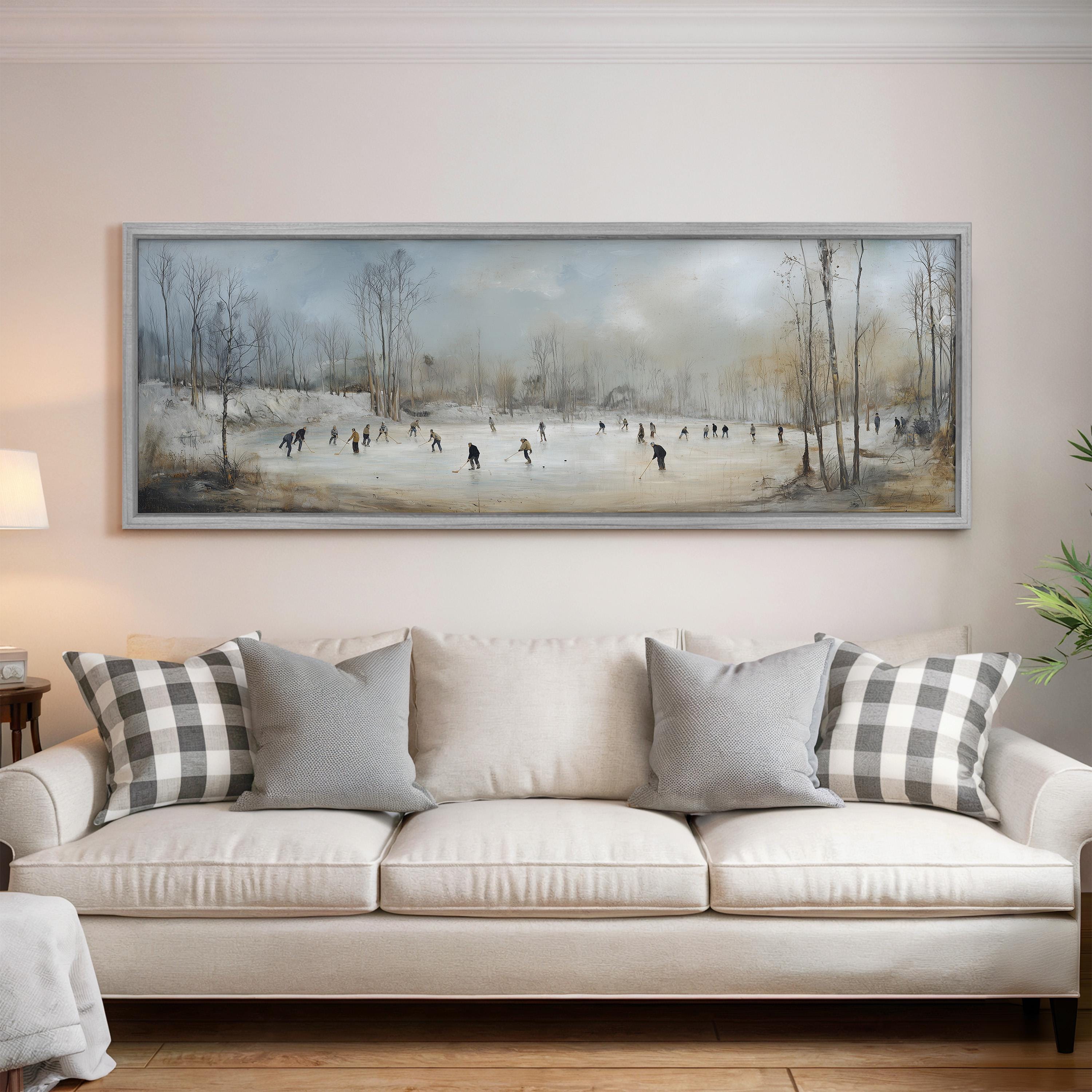 a large painting of people ice skating on a frozen pond, hanging on a wall above a white sofa with gray and white patterned pillows.
