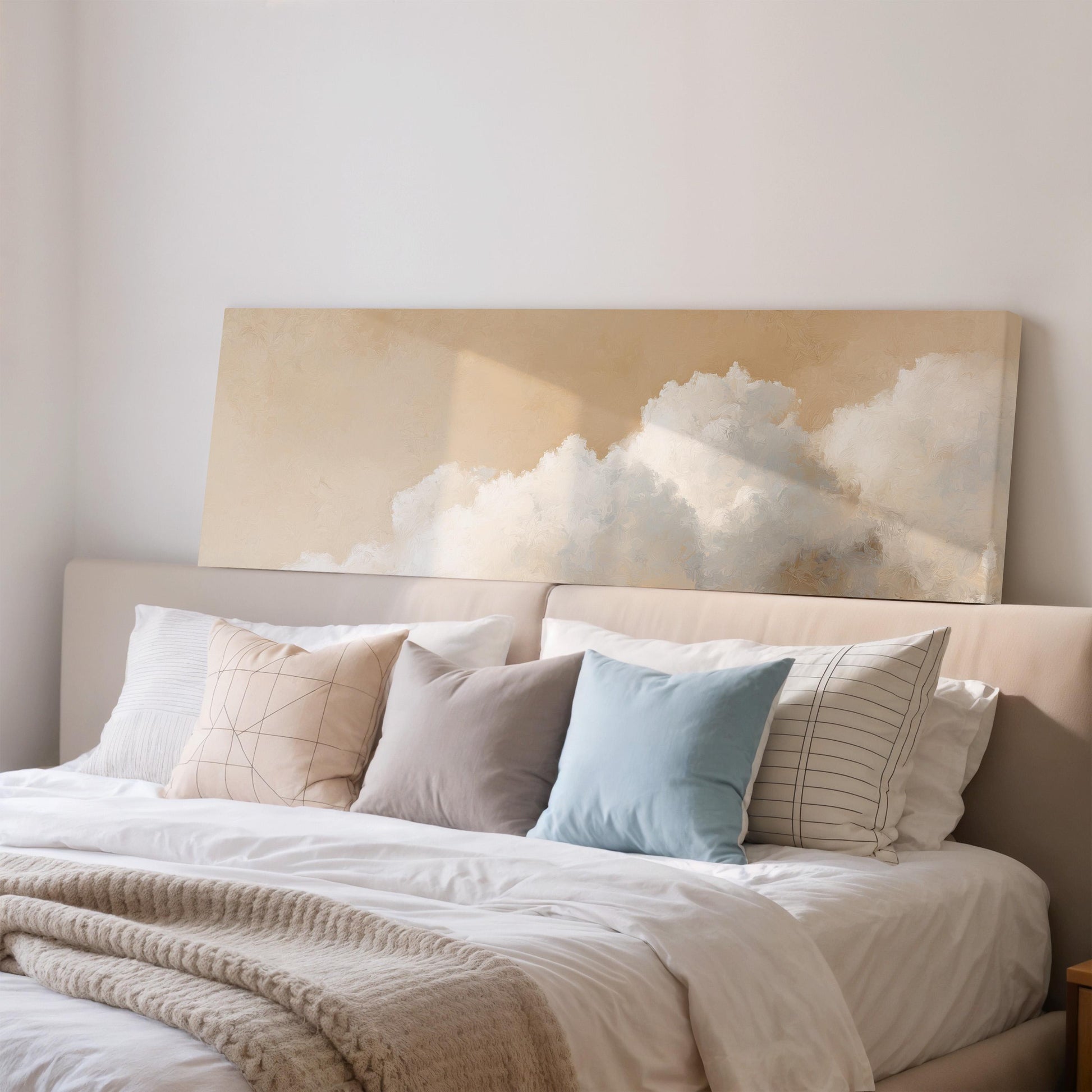 a cozy bedroom with a large bed adorned with white sheets and a blue pillow. Above the bed, there is a large canvas print depicting a cloud-filled sky, adding a serene and calming atmosphere to the room.